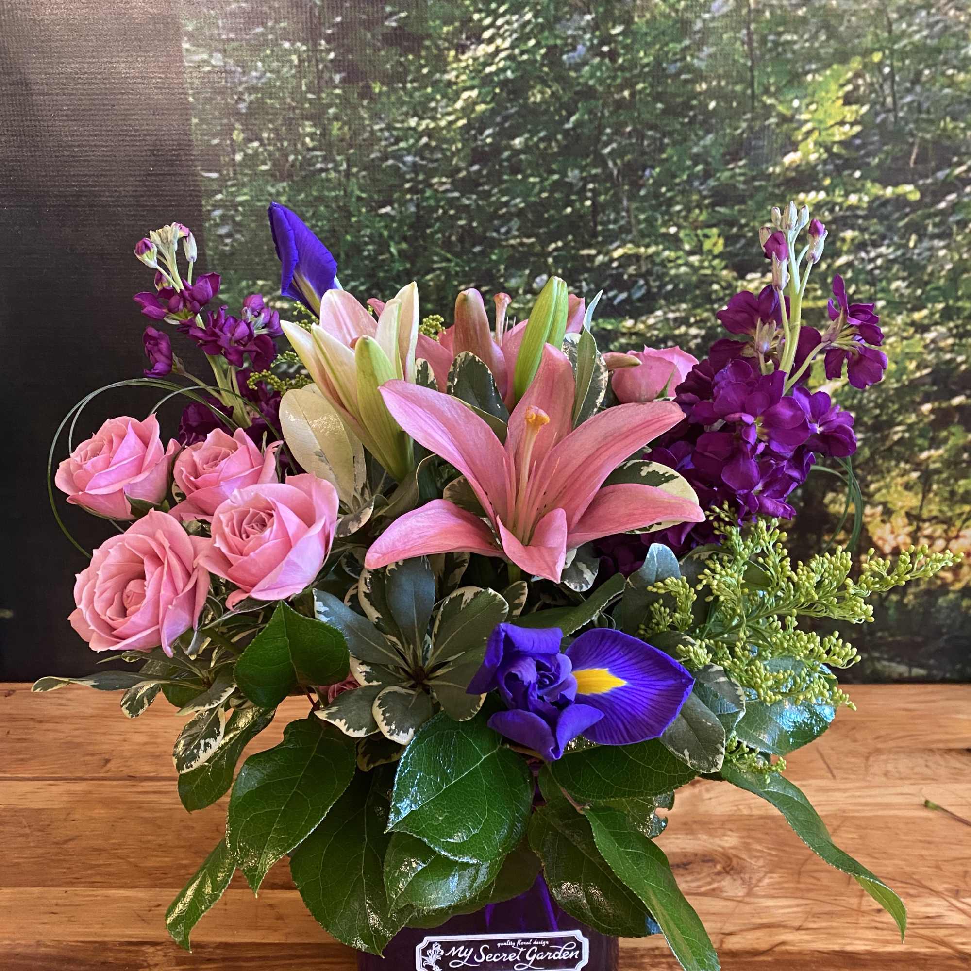 Pink roses, lilies, and purple flowers in a low vase arrangement