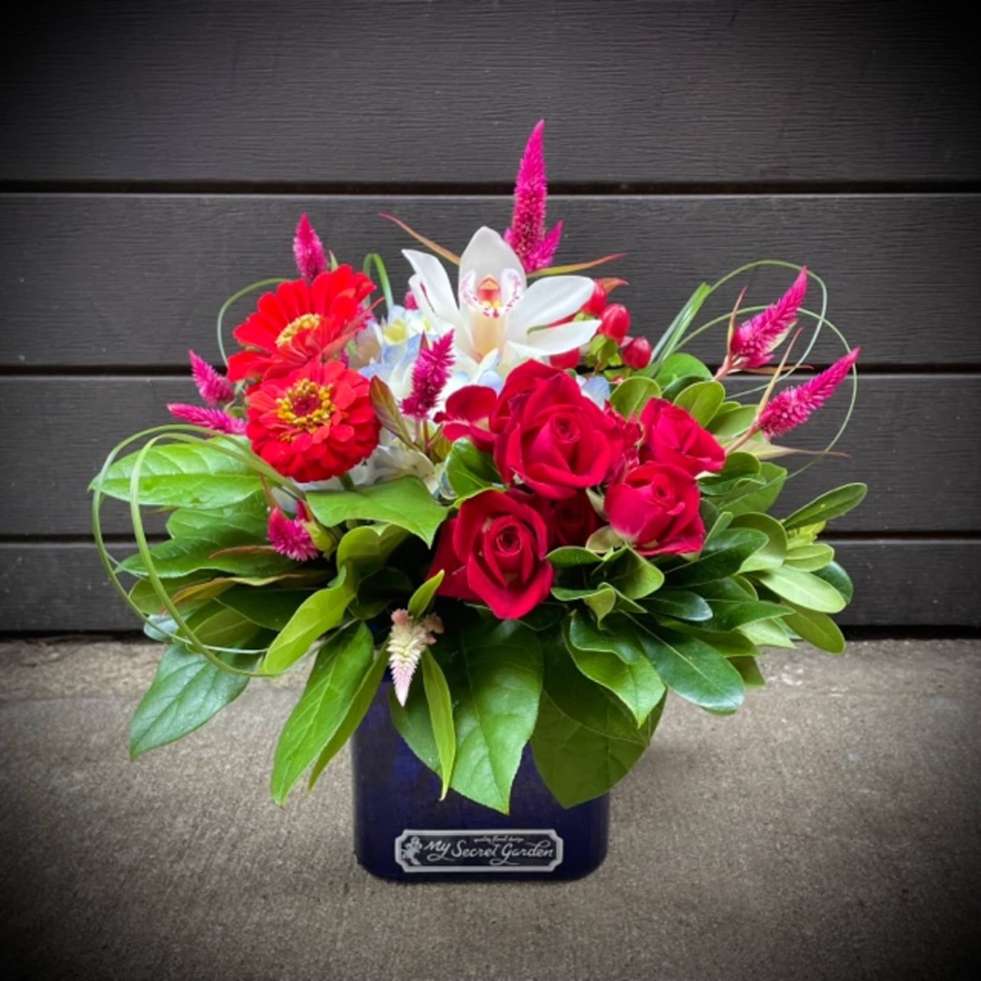 Red roses and white orchids in a dark vase with pink accents