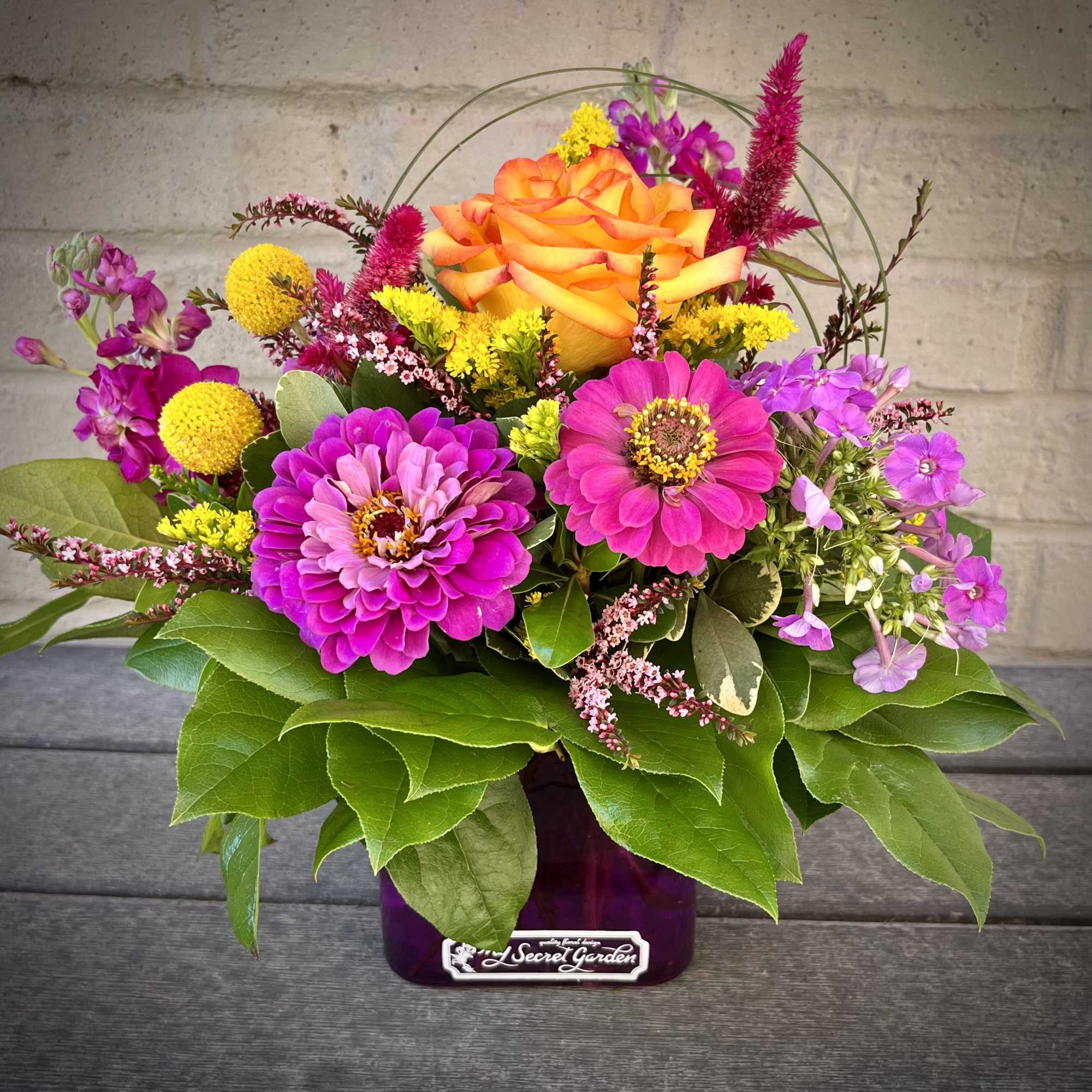 Bright mixed flower arrangement in a purple vase with orange and pink blooms