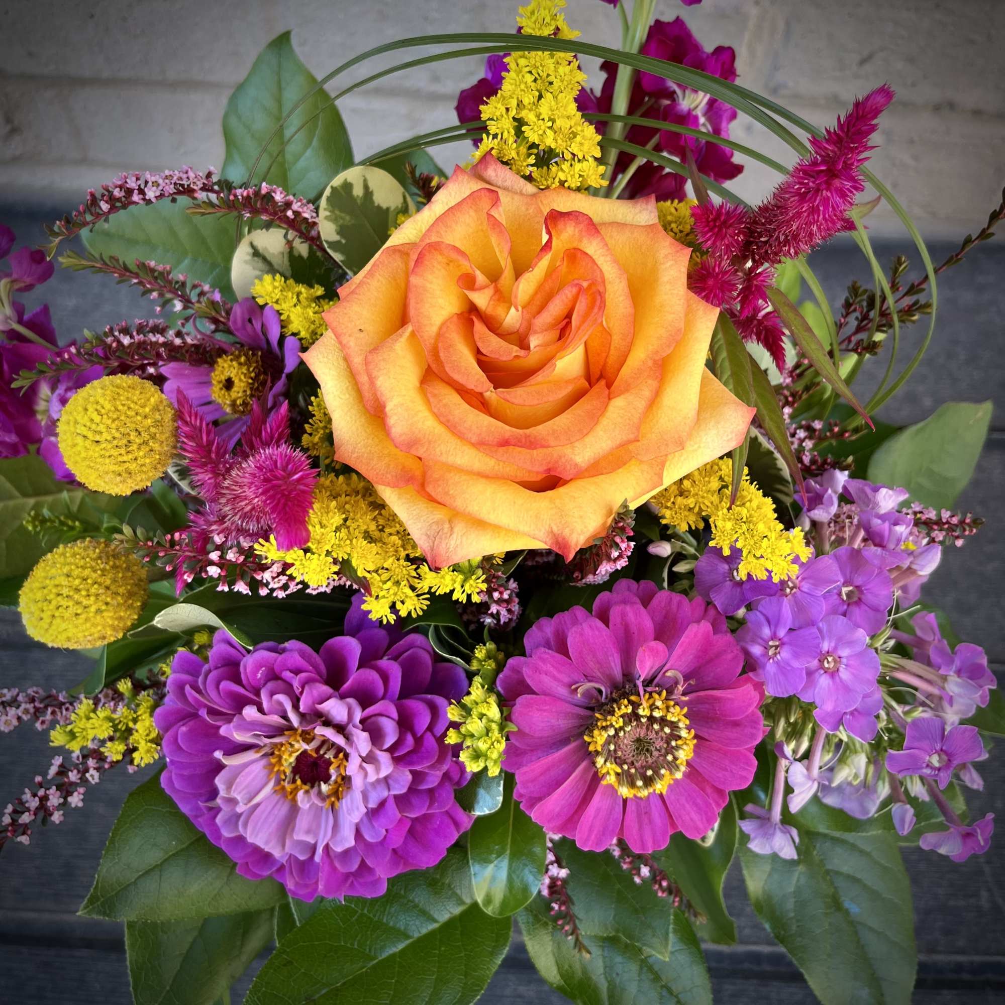 Mixed bouquet with an orange rose, purple blooms, and yellow accents