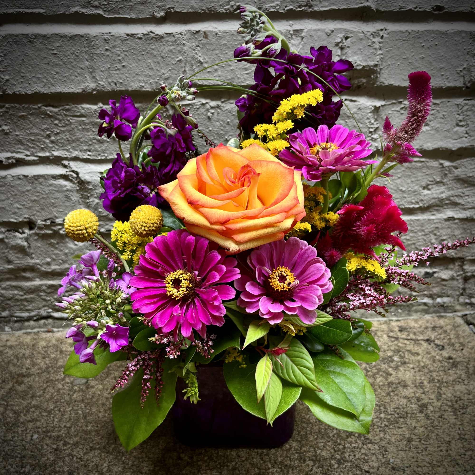 Mixed bouquet with an orange rose and bright pink flowers in a dark vase