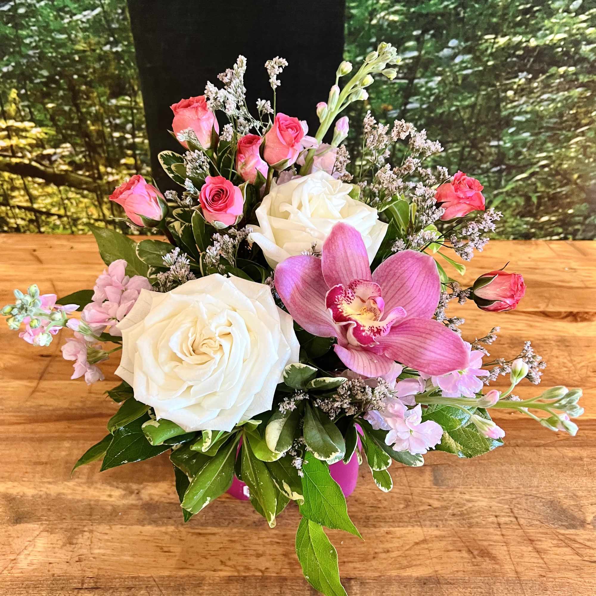Short arrangement of white roses, pink spray roses, and a pink orchid in a pink vase