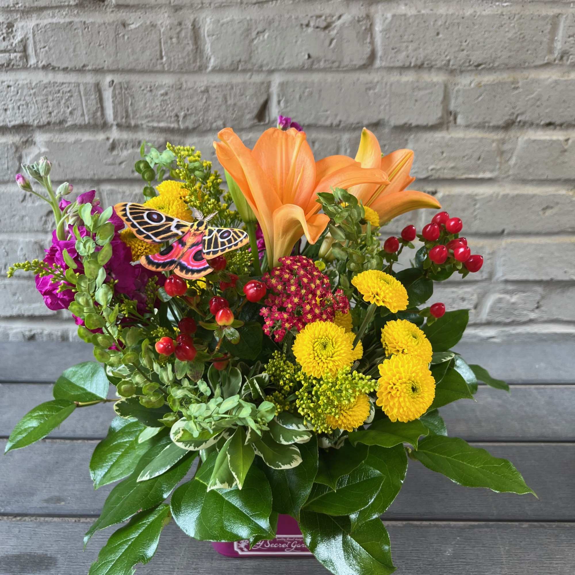 Orange lilies and yellow mums in a low container with a butterfly accent