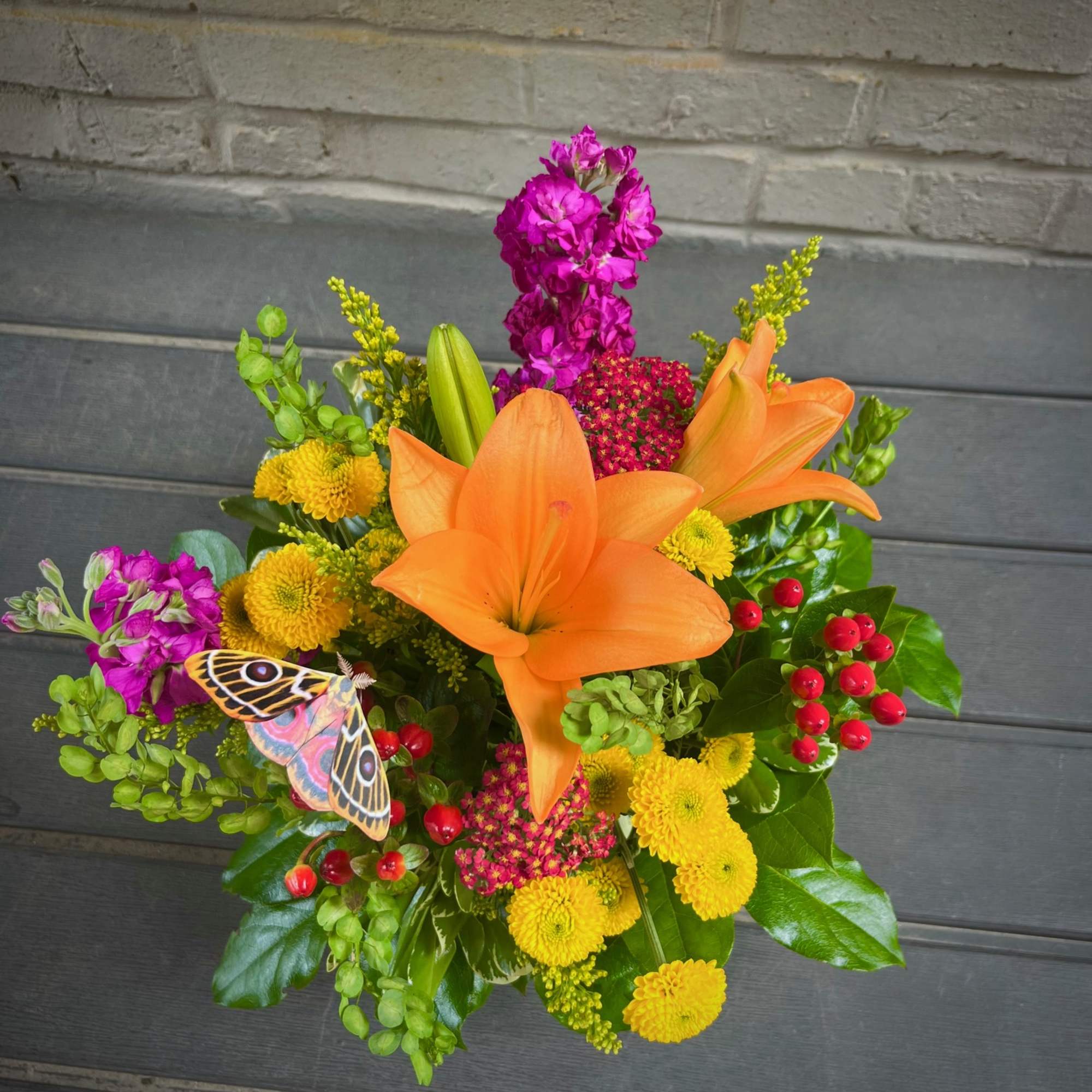 Bouquet with orange lilies, yellow mums, and magenta flowers with a butterfly accent