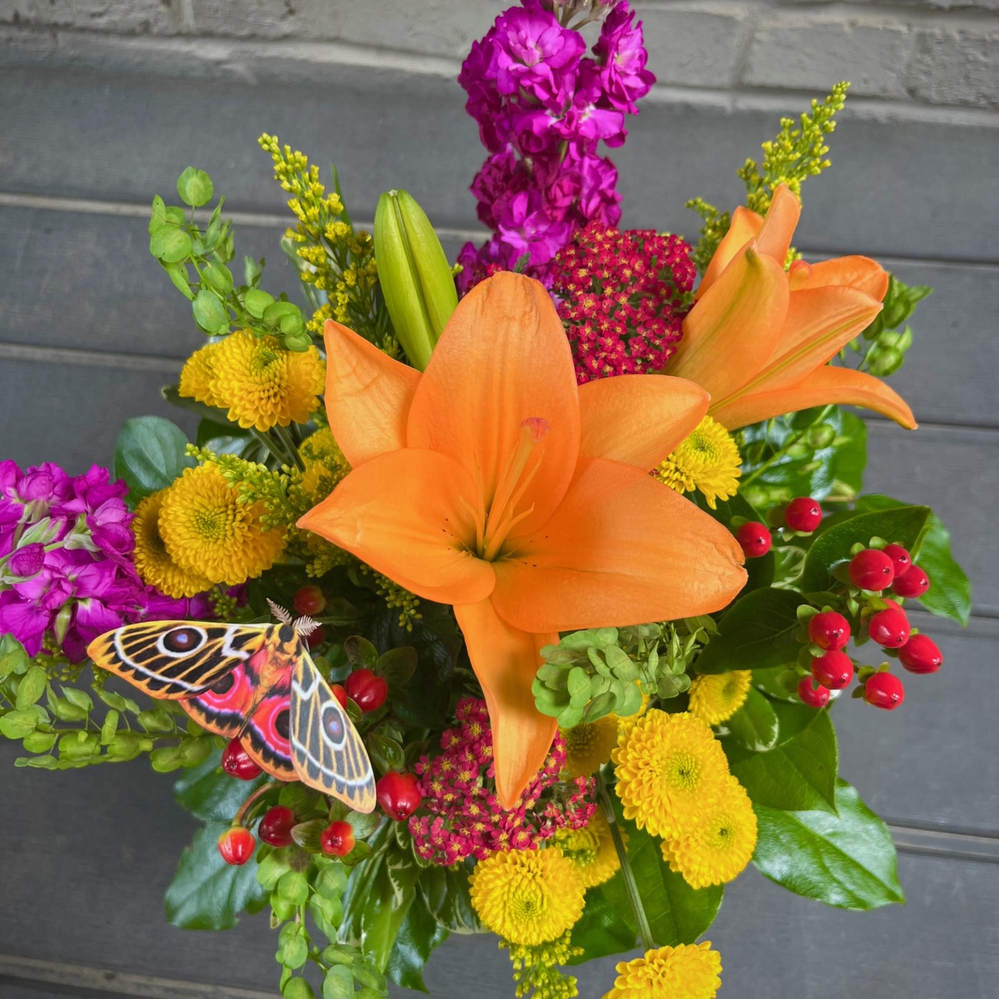 Bouquet of orange lilies, yellow mums, and purple flowers with a butterfly accent