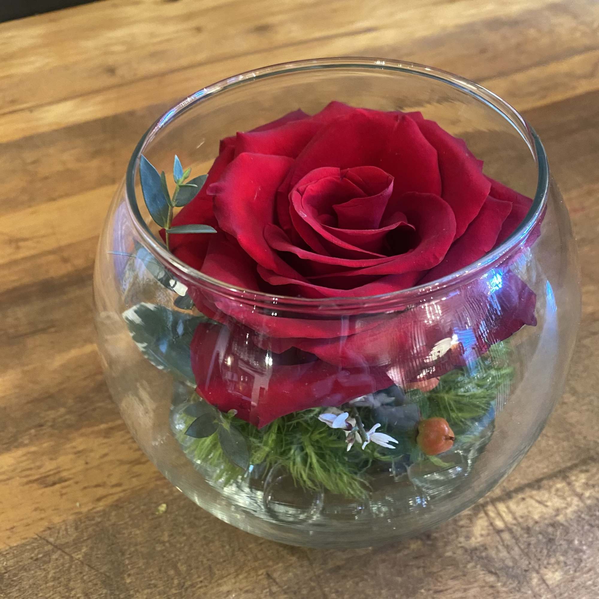 Single red rose in a round glass bowl with greenery