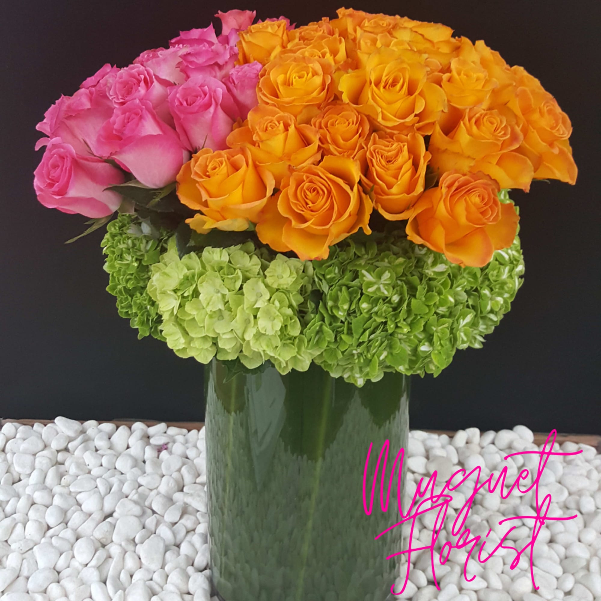 Pink and orange roses arranged in a tall glass vase with green hydrangeas