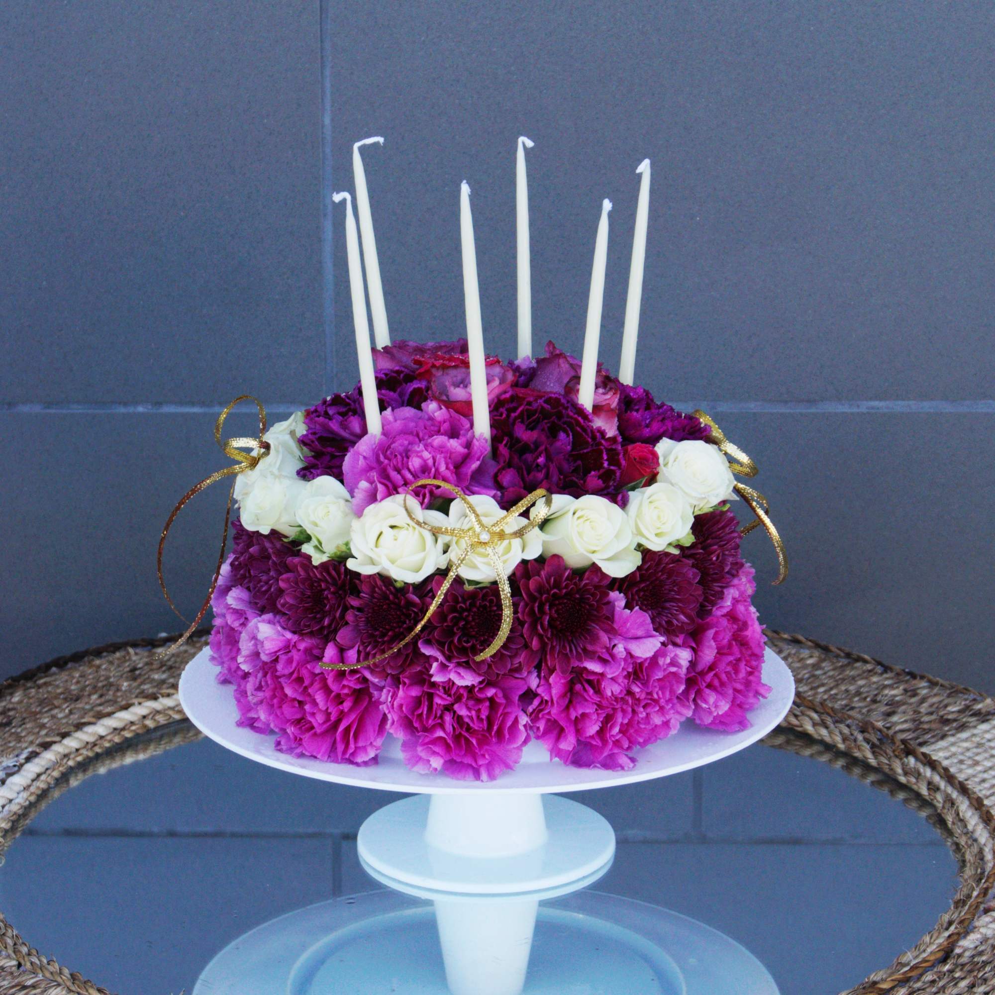 Round cake covered in pink and purple flowers with white candles