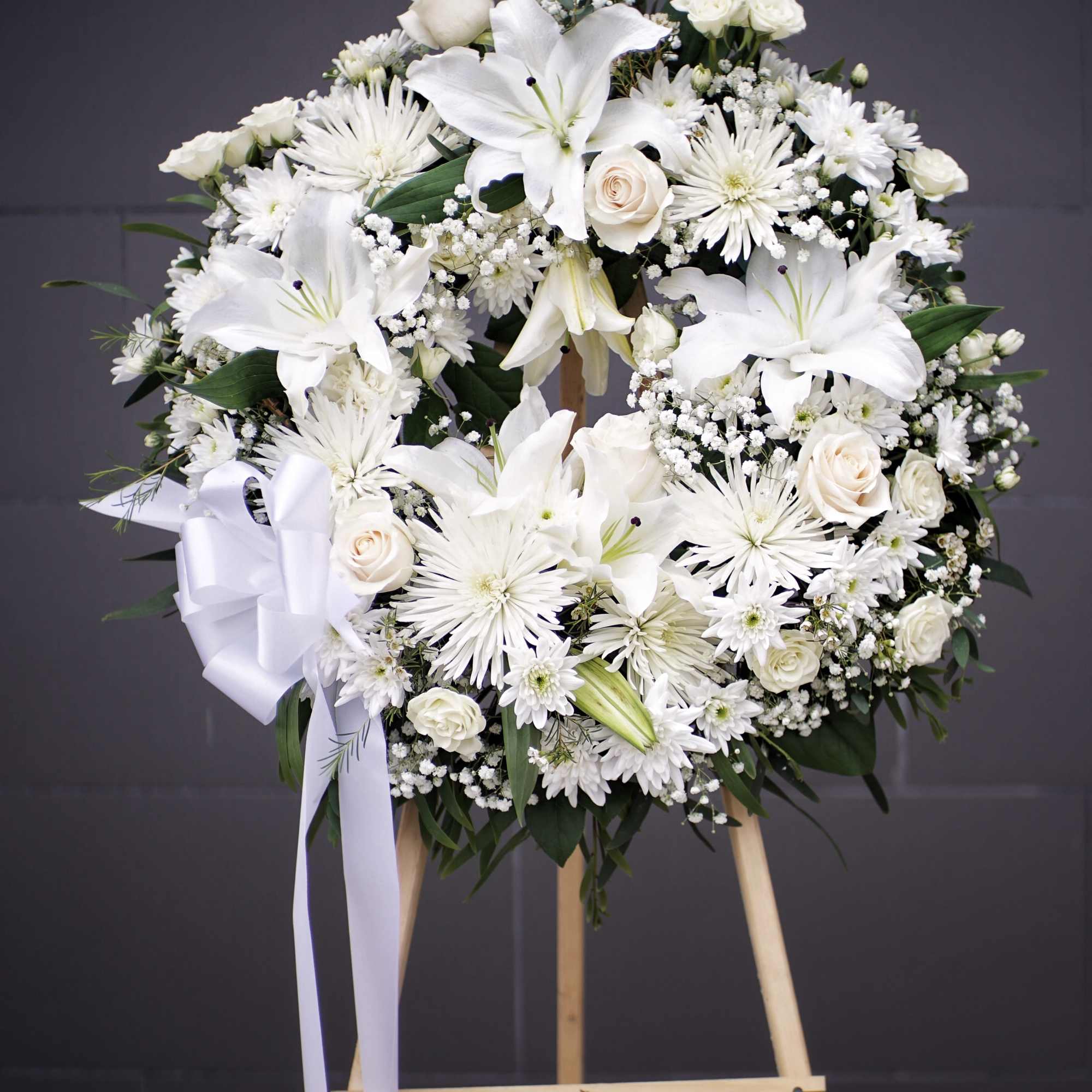 White floral wreath on a wooden easel with a ribbon bow