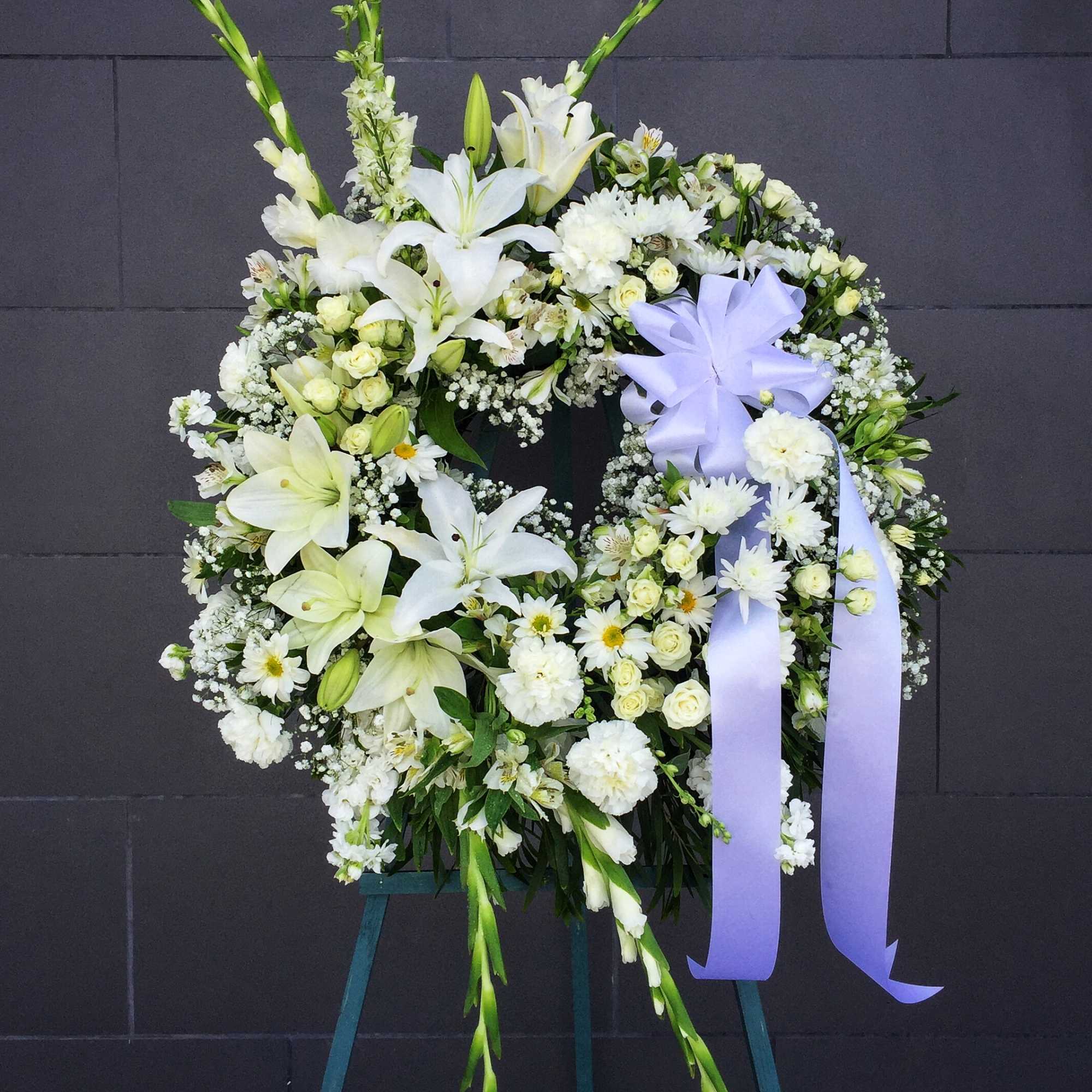 White floral wreath on an easel with a lavender ribbon