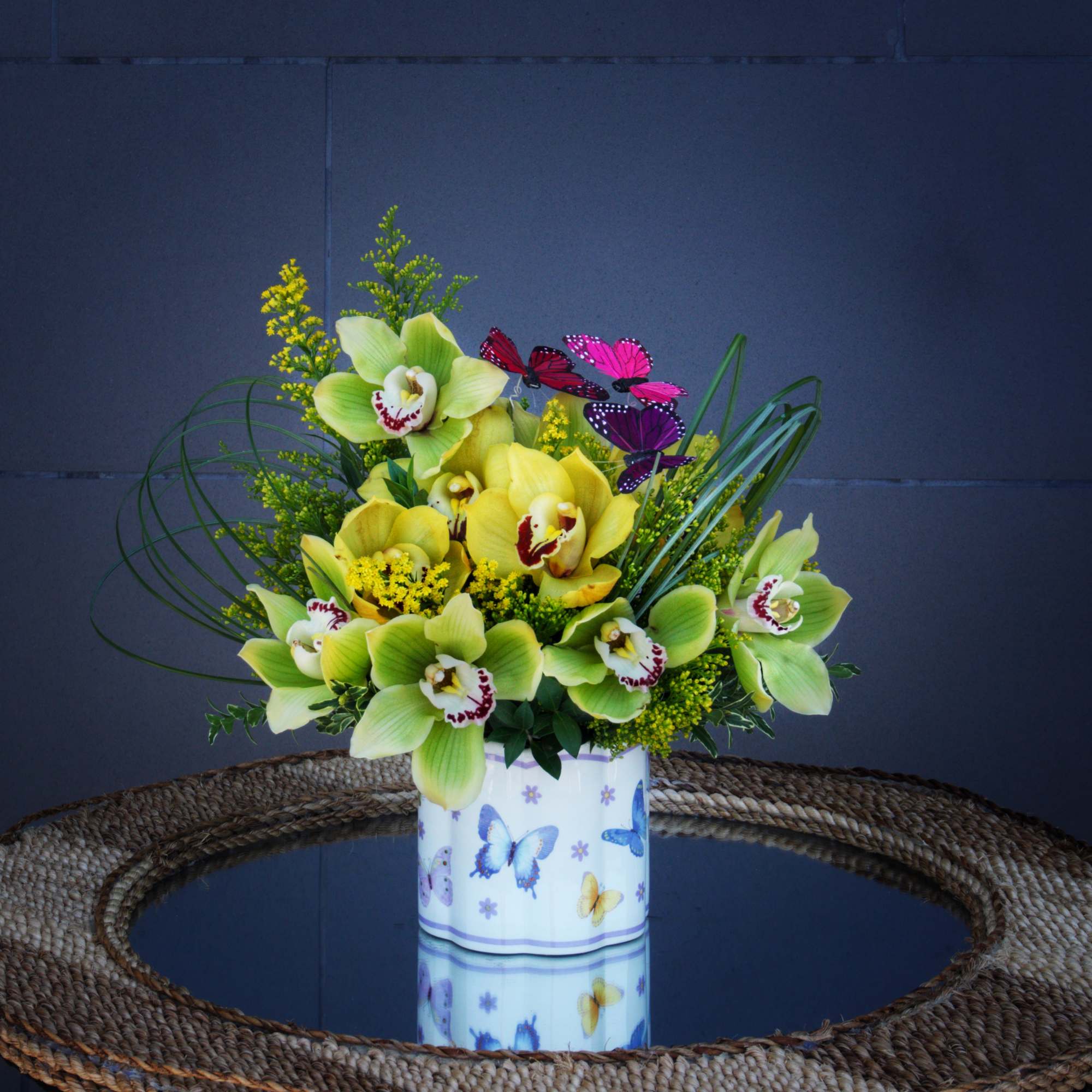 Yellow and green orchid arrangement in a butterfly-decorated container