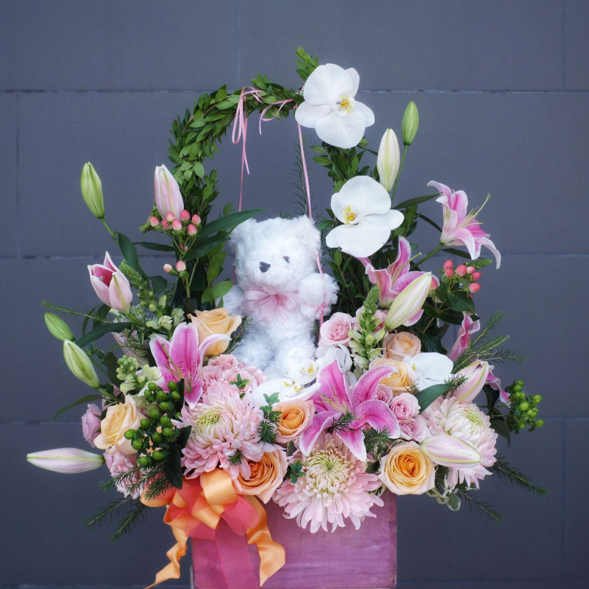 Floral arrangement with pink lilies, roses, and a teddy bear in a purple box