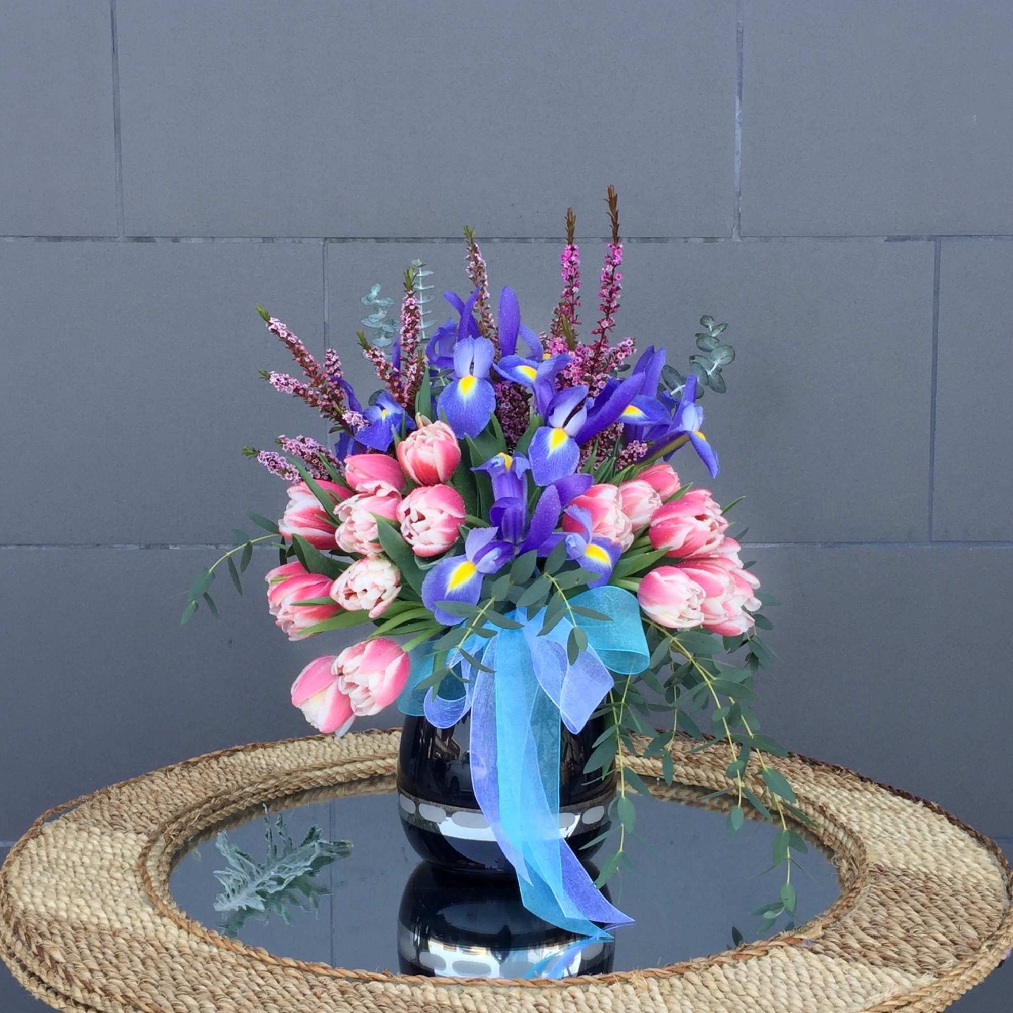 Bouquet of pink tulips and purple irises in a black vase with a blue ribbon