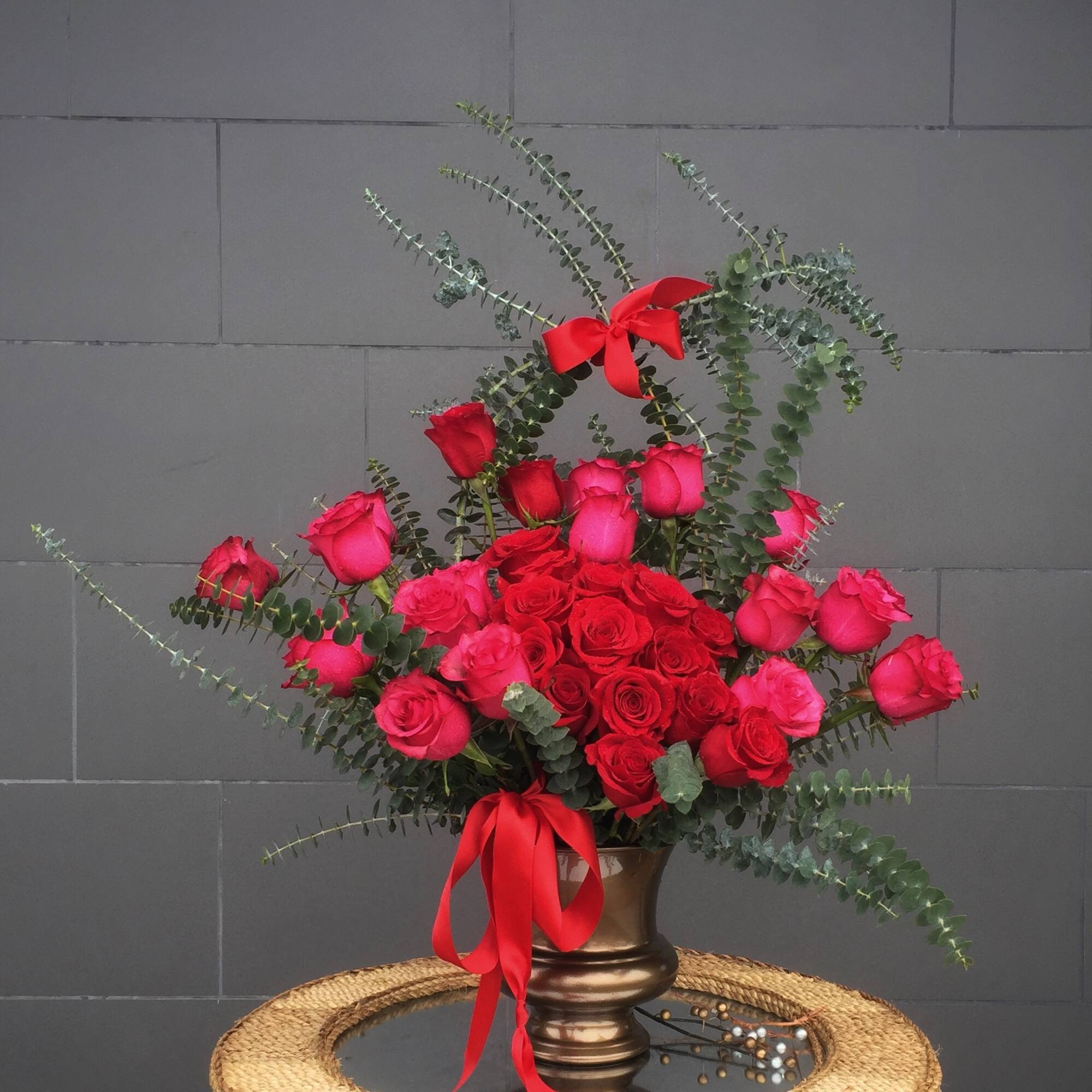 Red and pink rose arrangement in a bronze vase with red ribbon