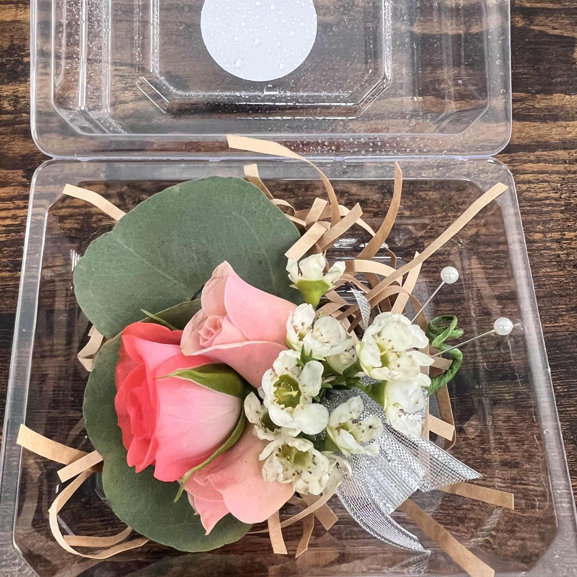 Three rose buds in a clear plastic box with small white flowers