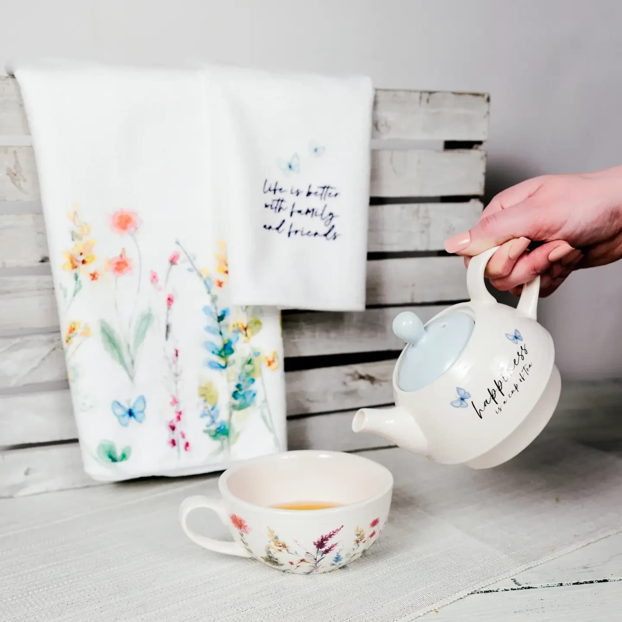 Floral-print mug, teapot, and towel gift set on a white wooden surface