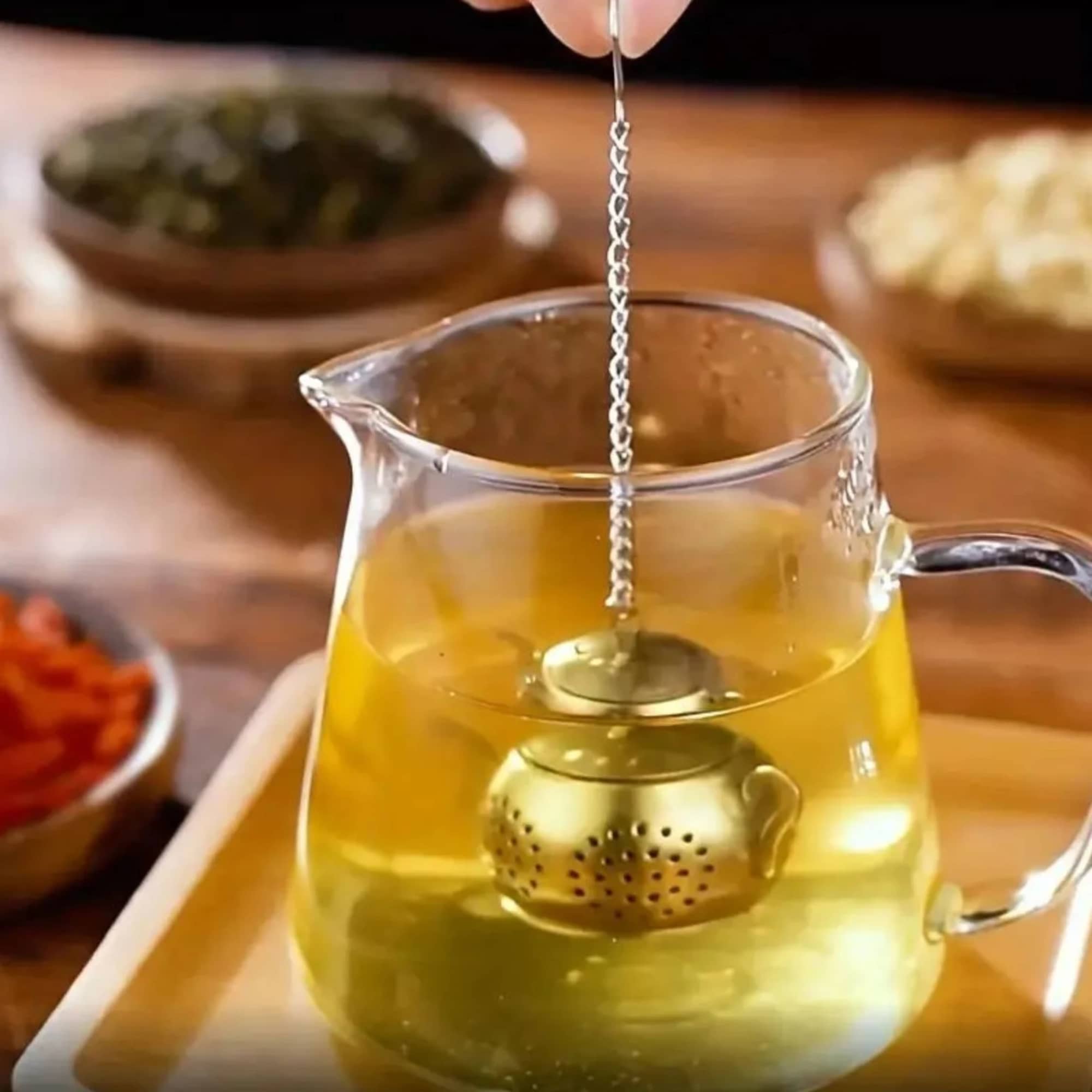 Glass teapot with yellow tea and a metal infuser on a tray