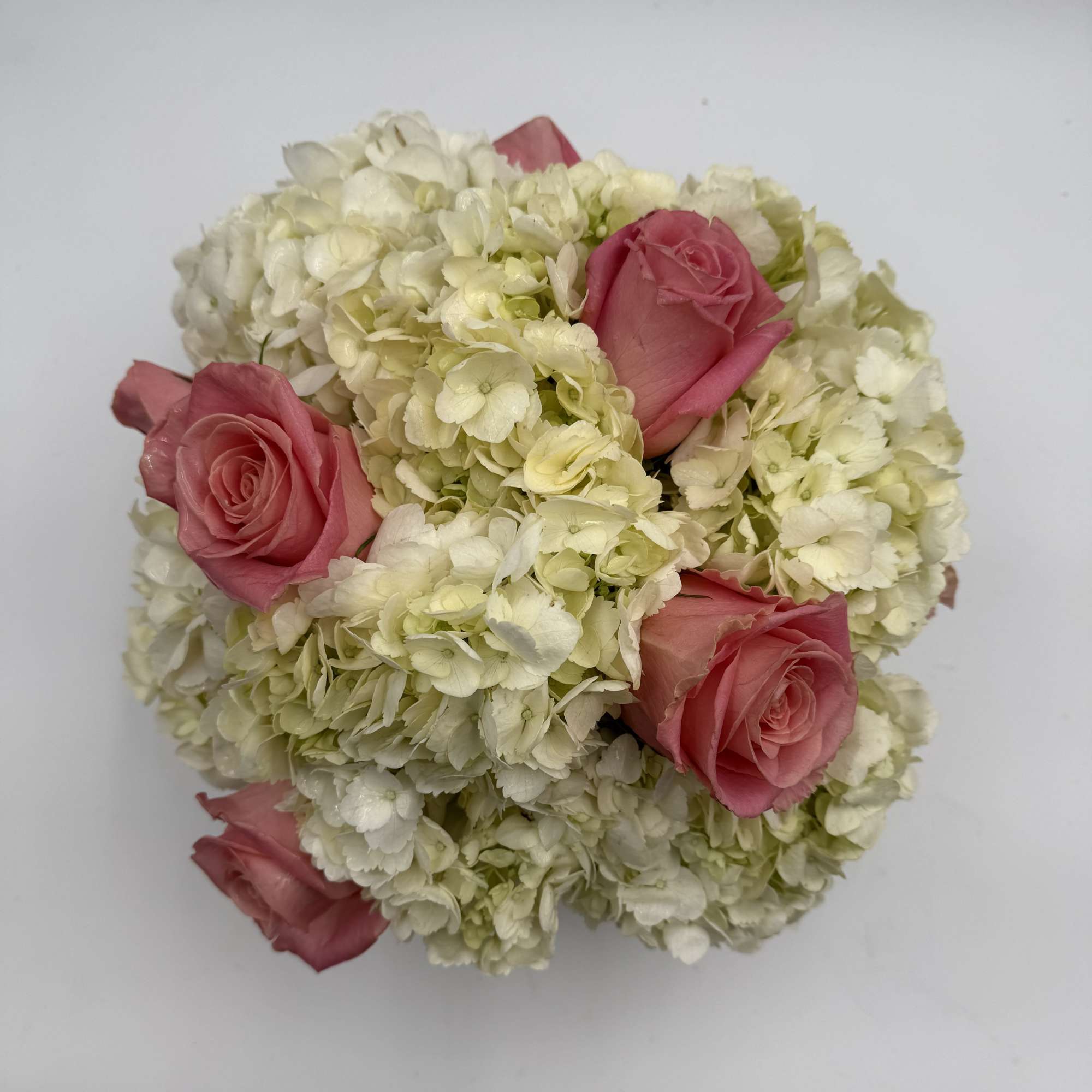 Pink roses nestled in a round cluster of white hydrangeas