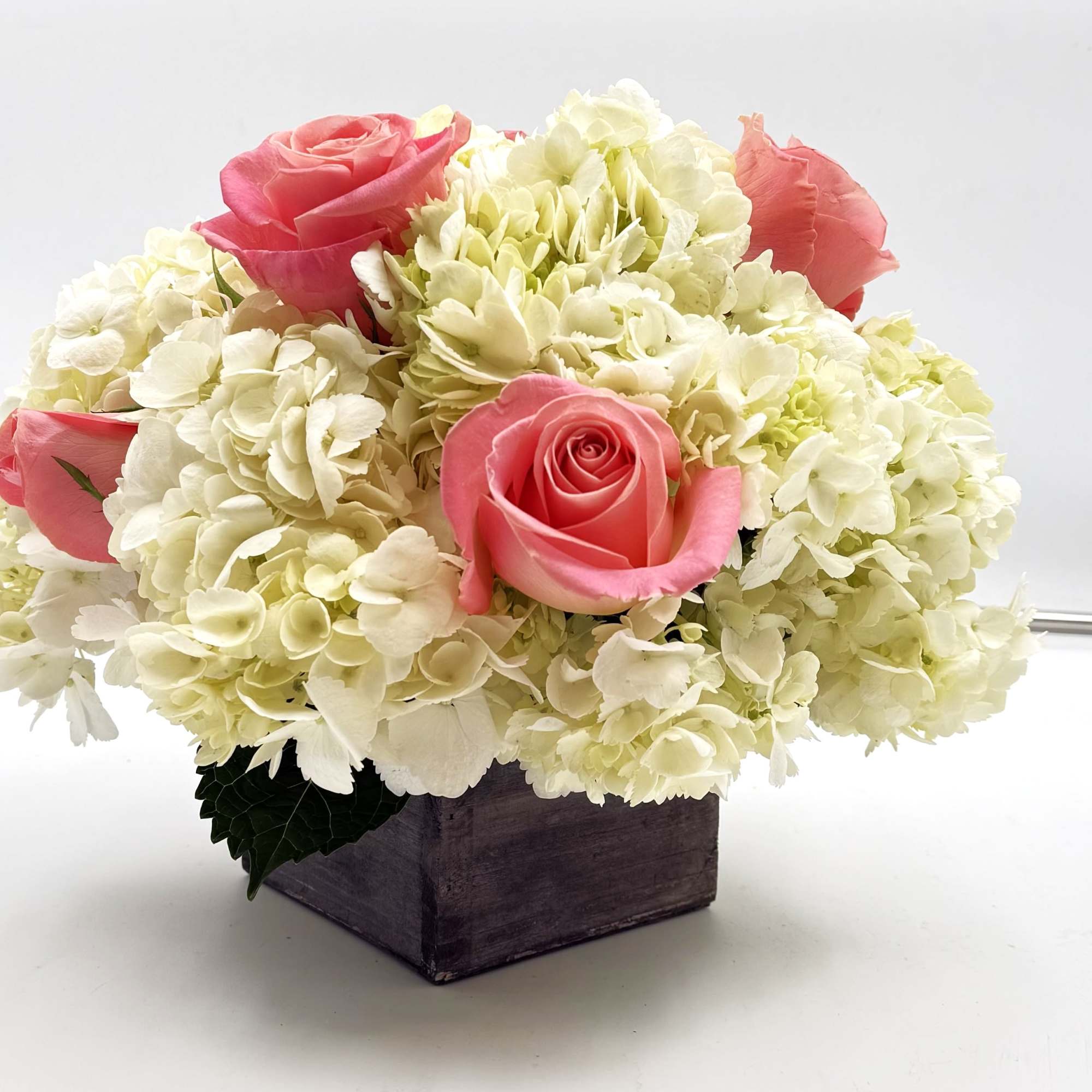Pink roses arranged with white hydrangeas in a wooden box