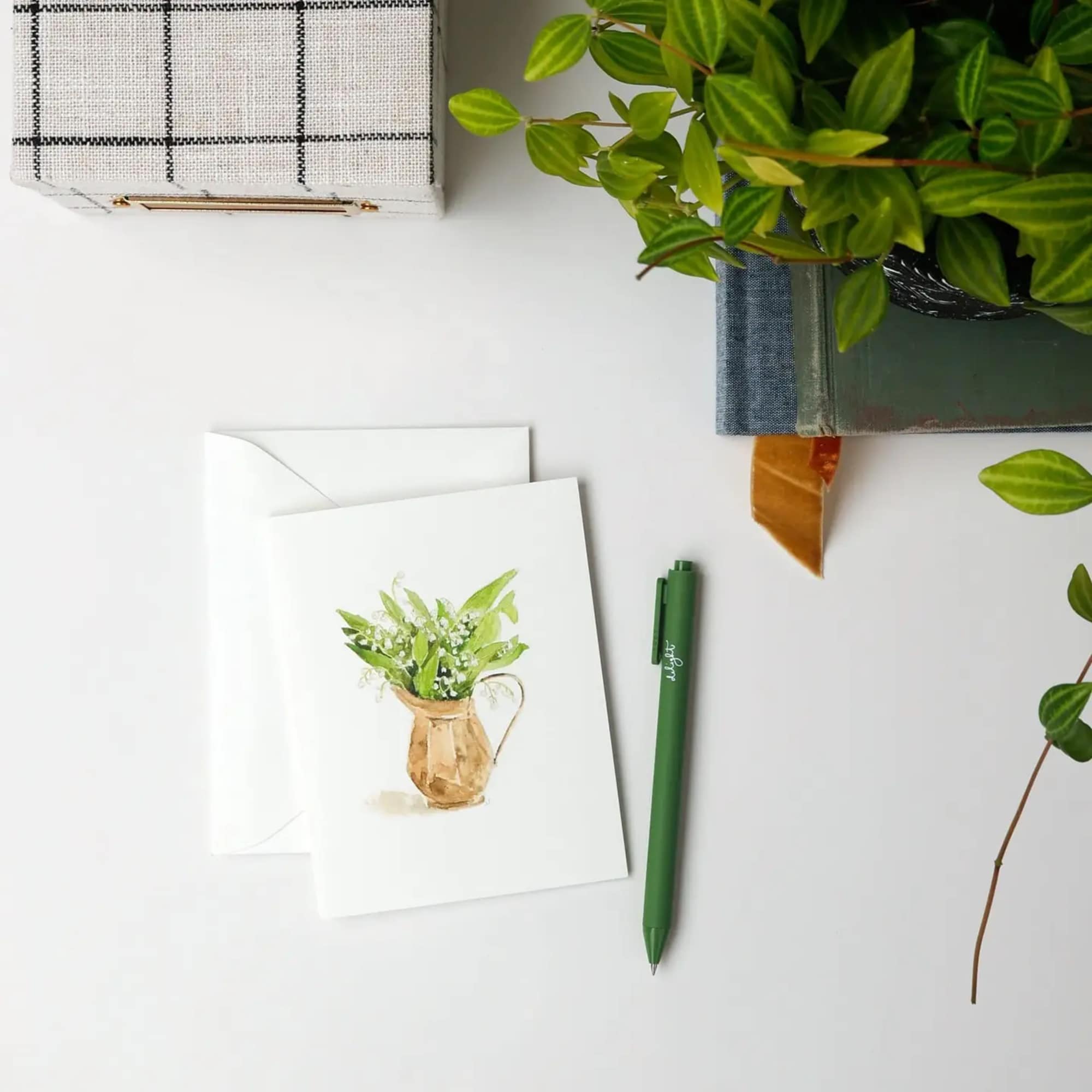 Greeting card with a watercolor potted plant illustration beside an envelope and pen