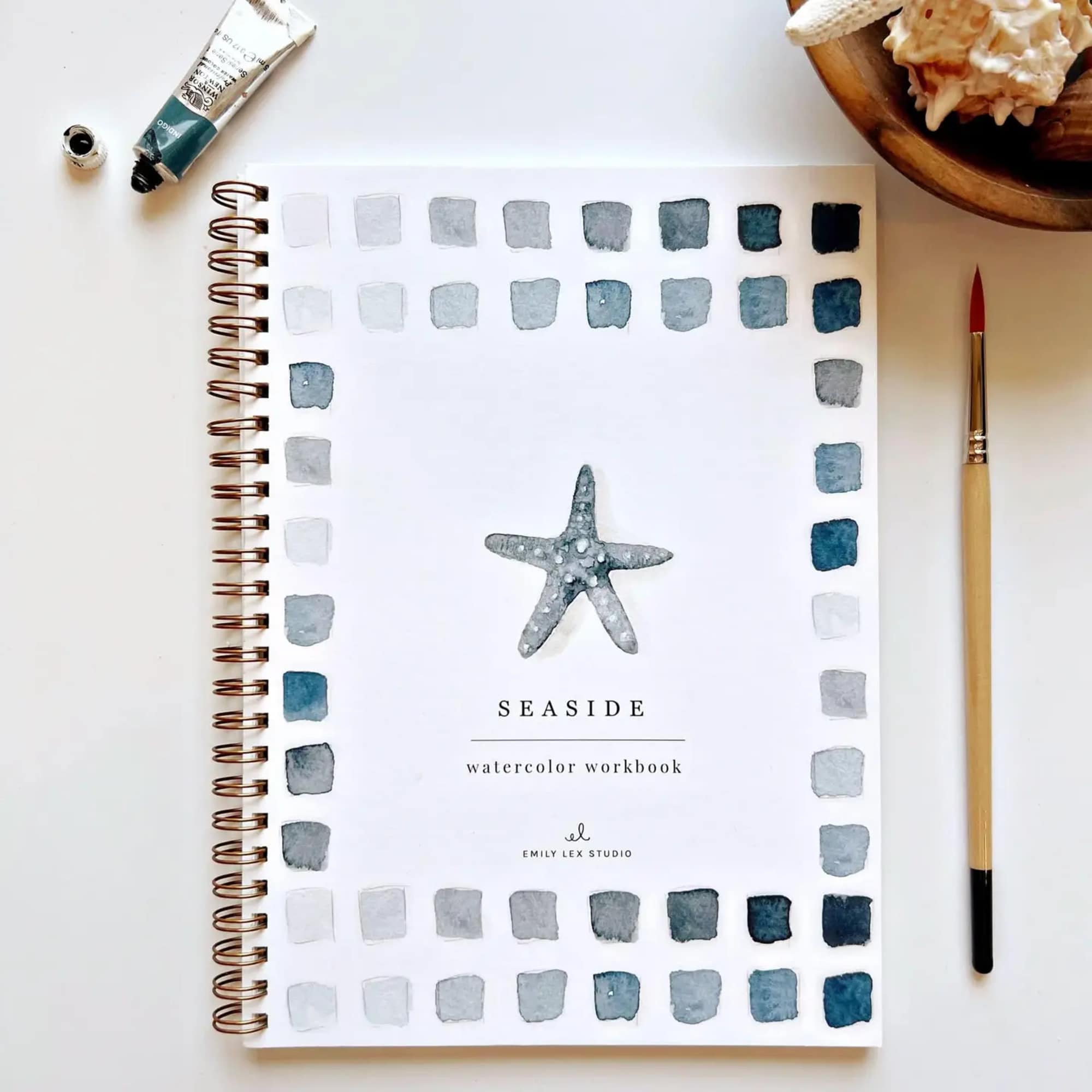 Watercolor workbook with a starfish cover and paintbrush beside it