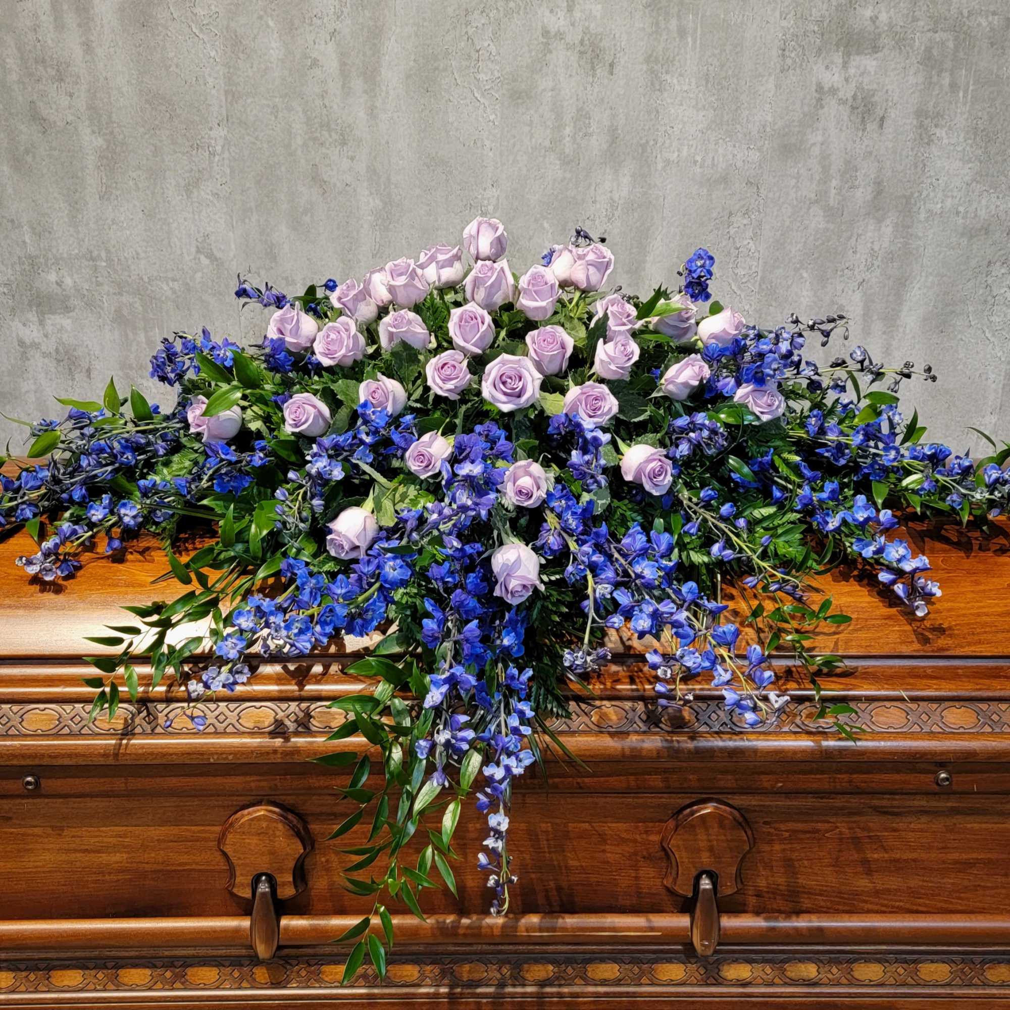 Lavender roses and blue flowers arranged on a wooden casket