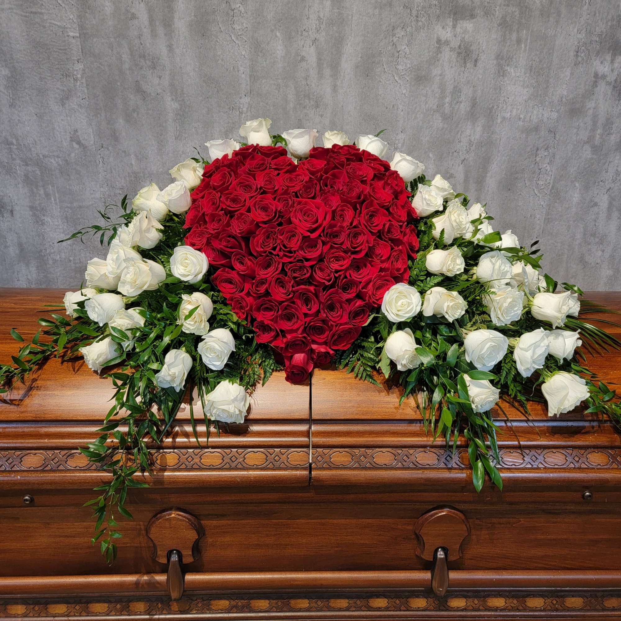 Heart-shaped red rose arrangement with white roses on a casket