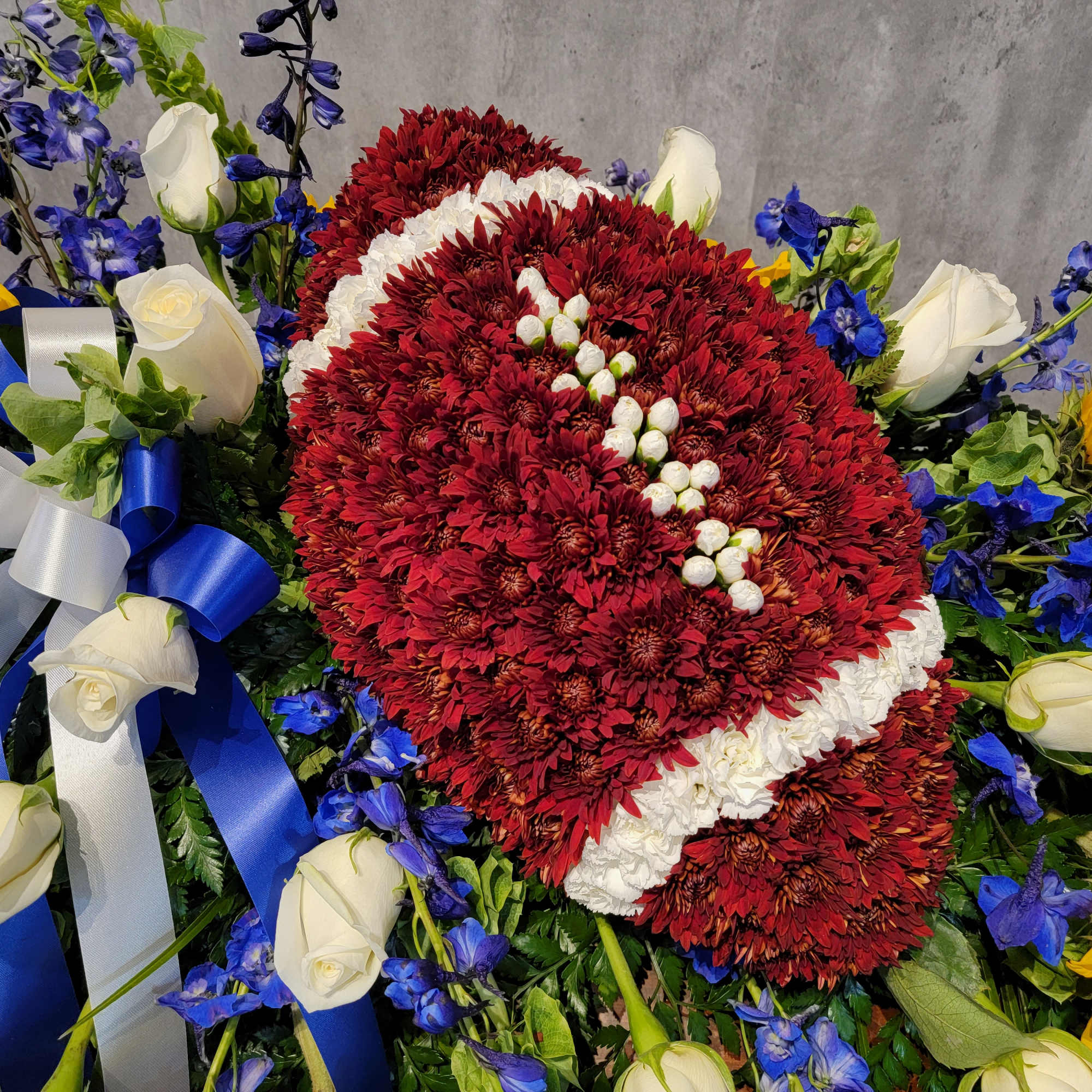 Red chrysanthemum wreath with white roses, blue flowers, and ribbon bows