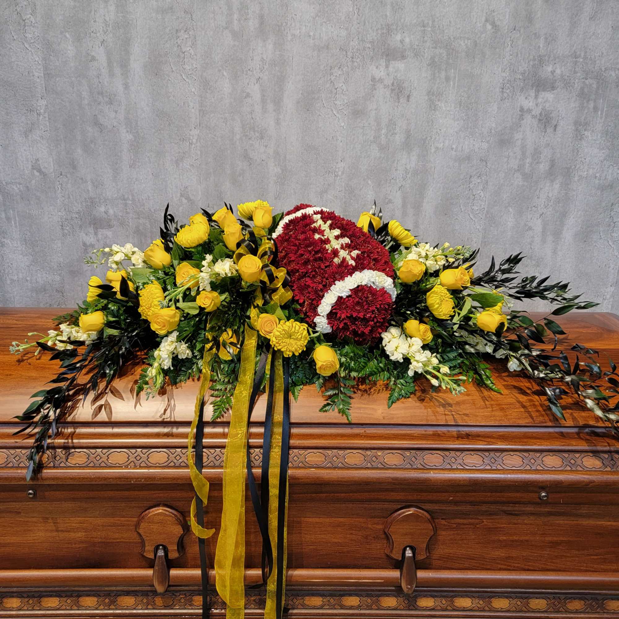 Red and white floral casket spray with yellow roses on a wooden casket