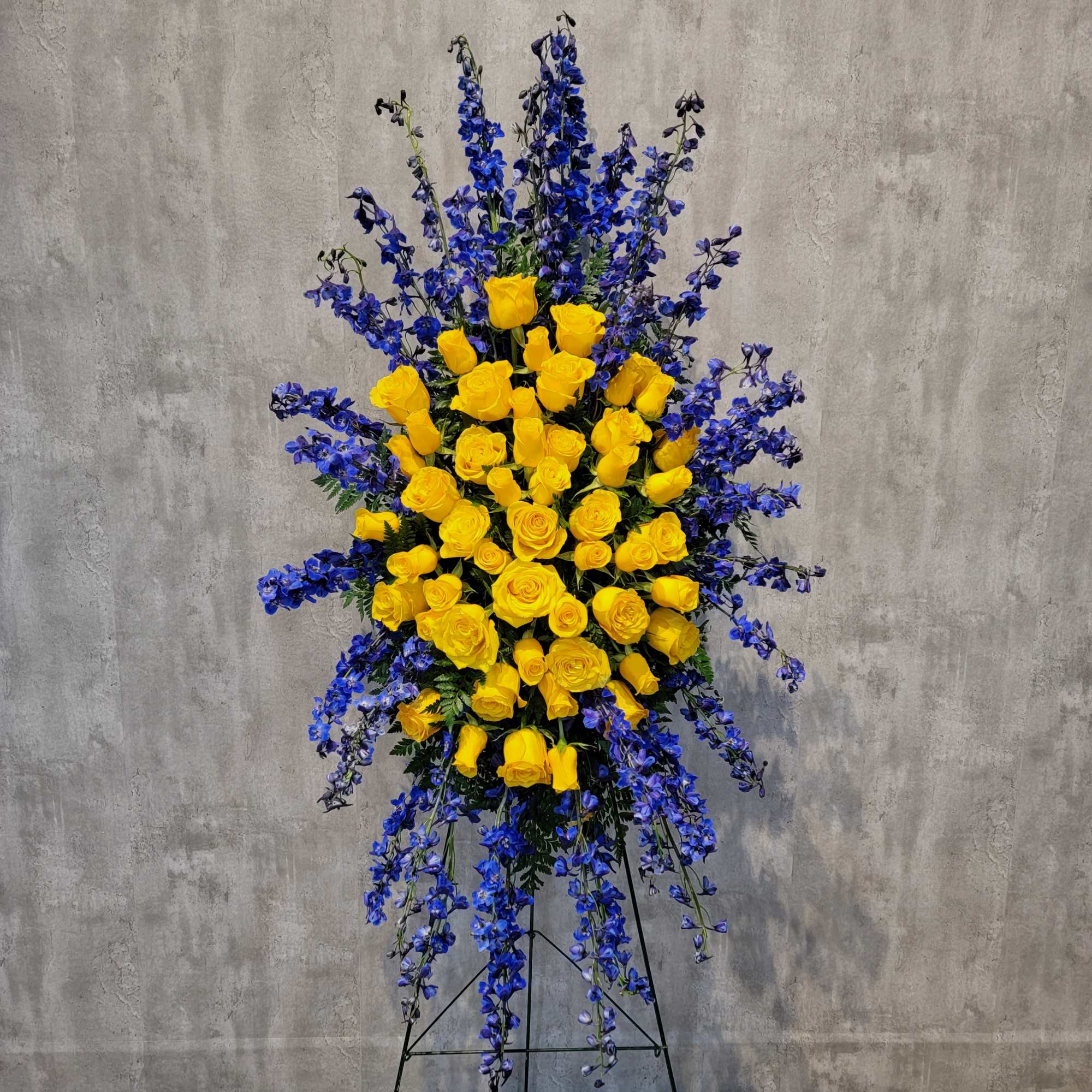 Tall standing arrangement of yellow roses and blue flowers on a black easel