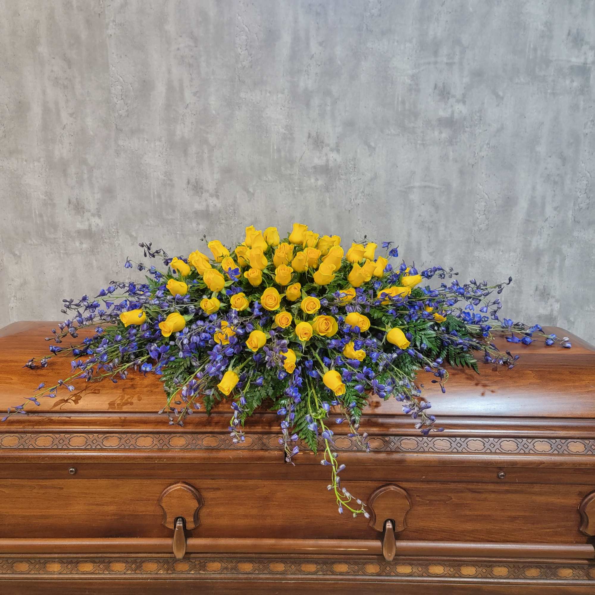 Yellow roses and purple flowers arranged on a wooden casket