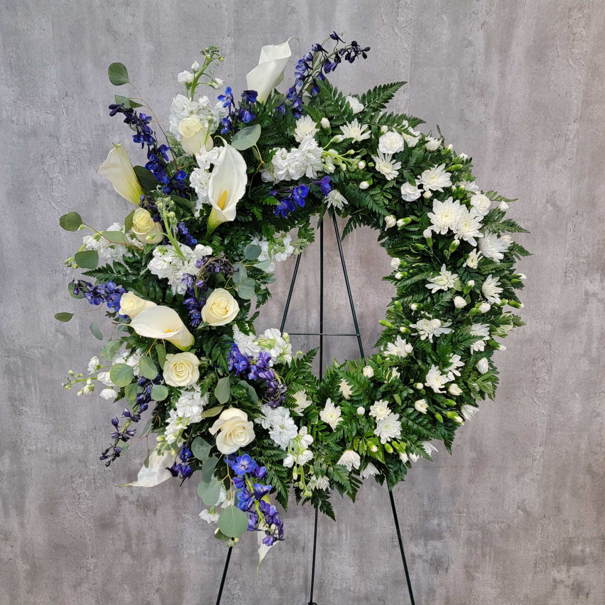 Large white and blue floral wreath on a black stand