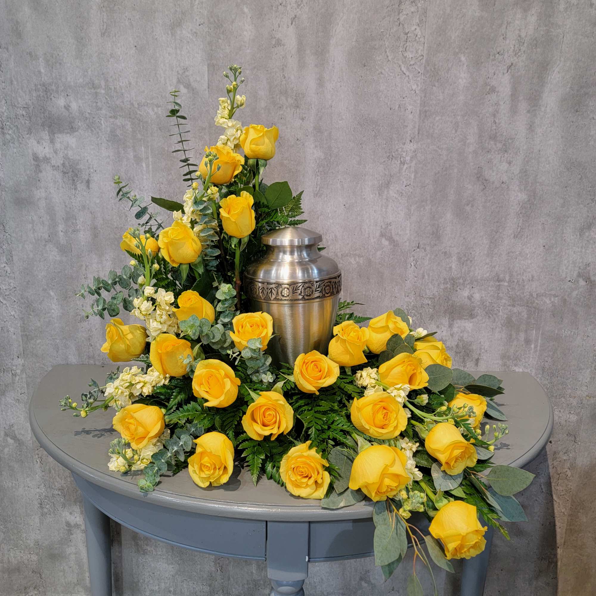 Yellow rose funeral arrangement around a silver urn