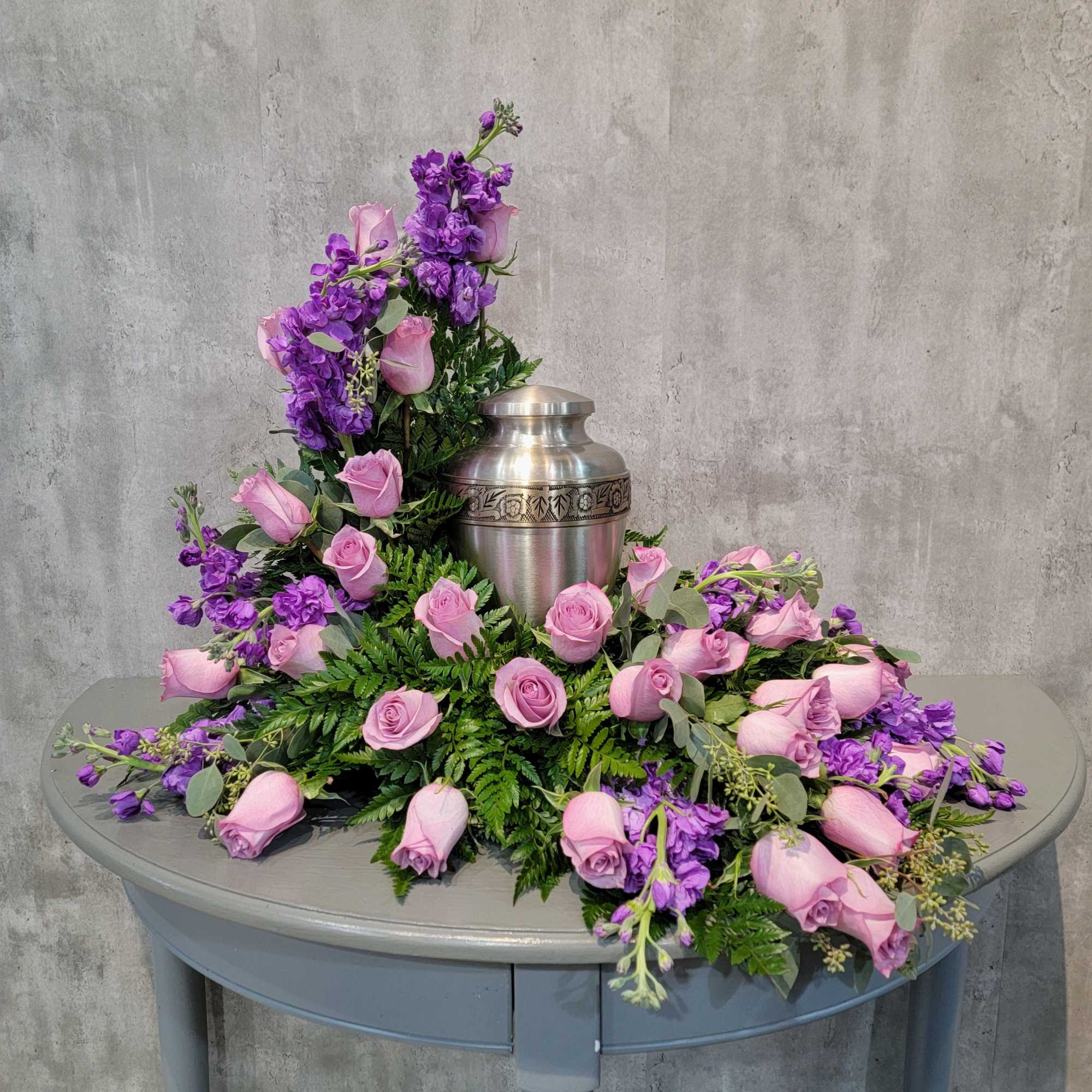 Pink roses and purple flowers arranged around a silver urn.