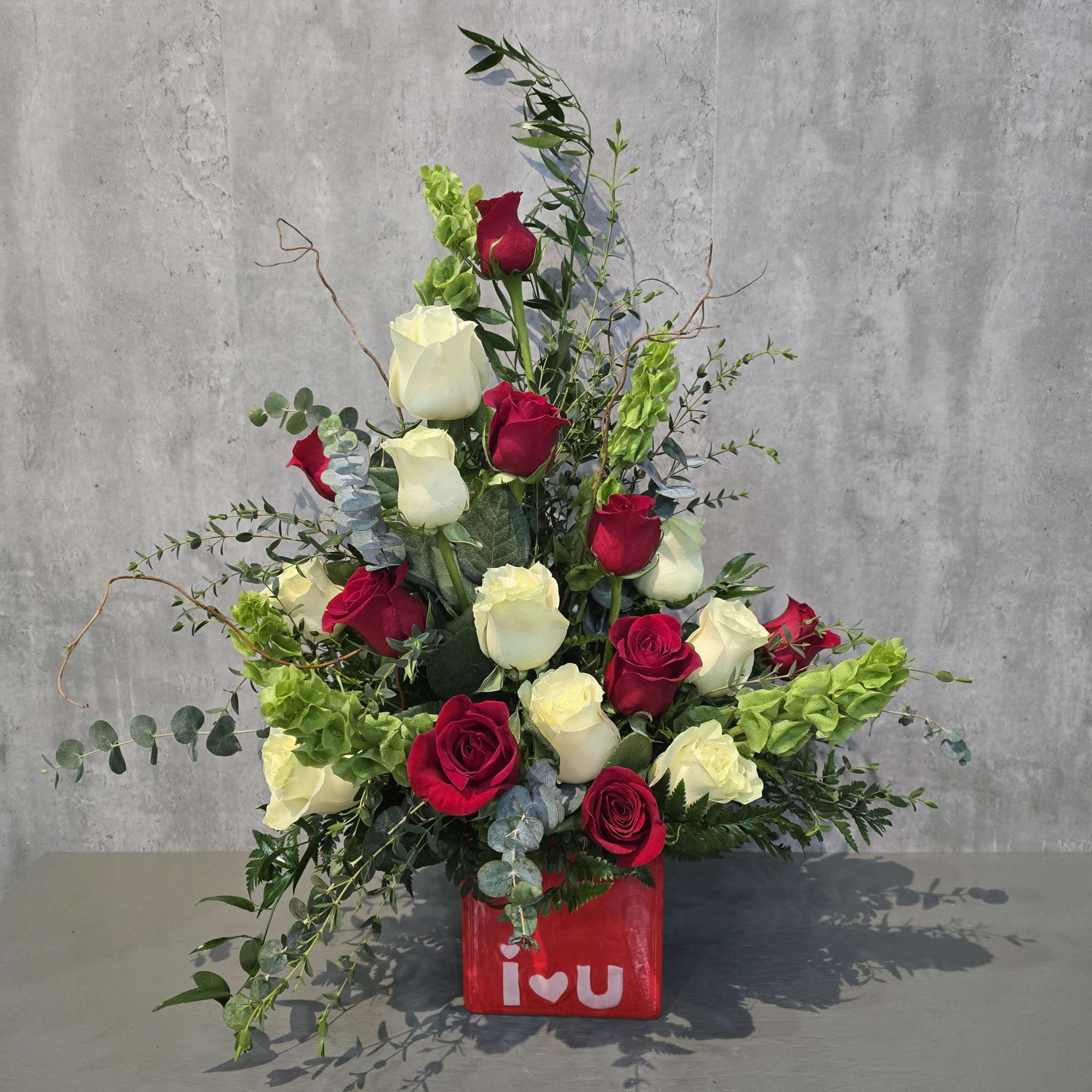 Red and white roses in a red cube vase with "i love u" text
