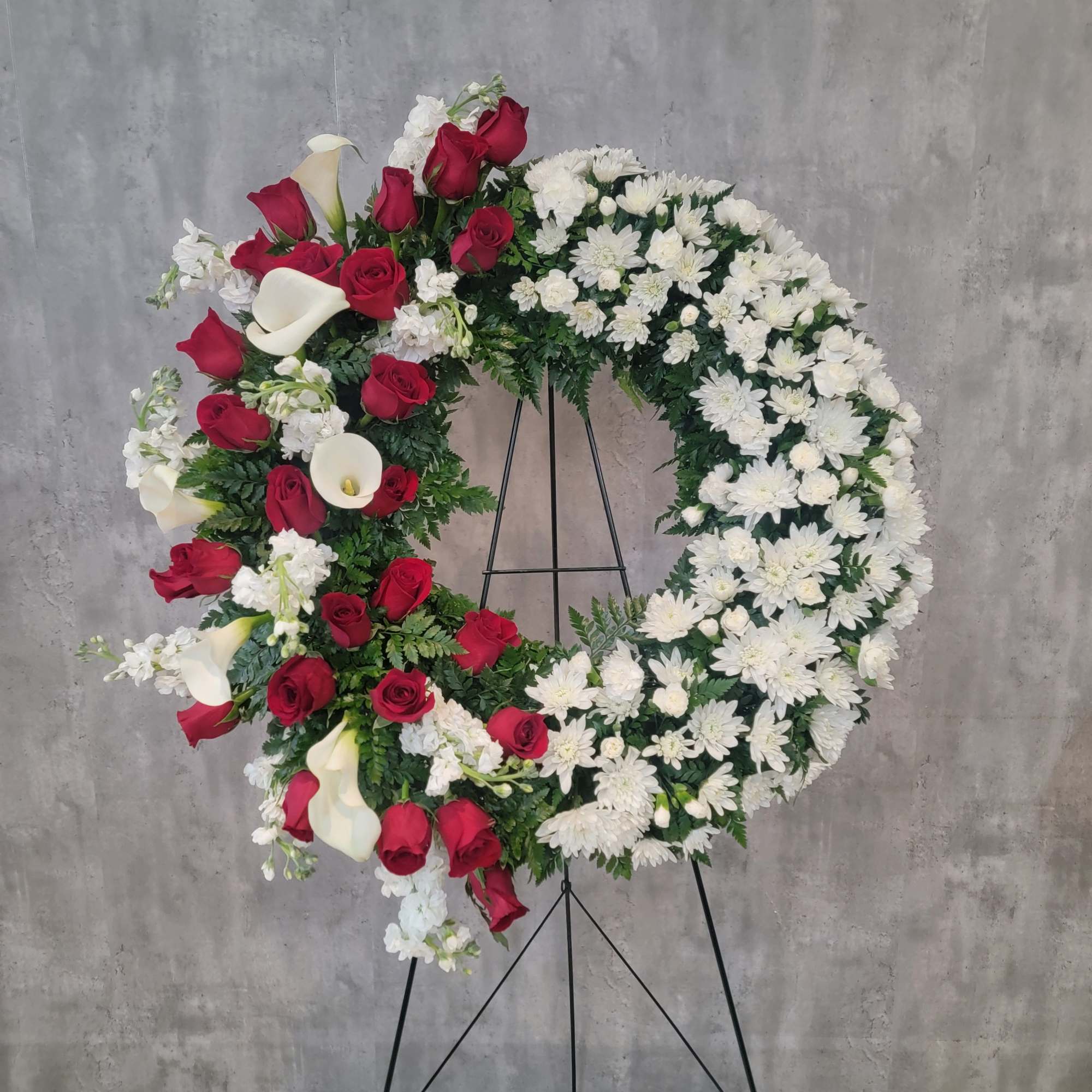 Circular funeral wreath with red roses, white daisies, and white calla lilies