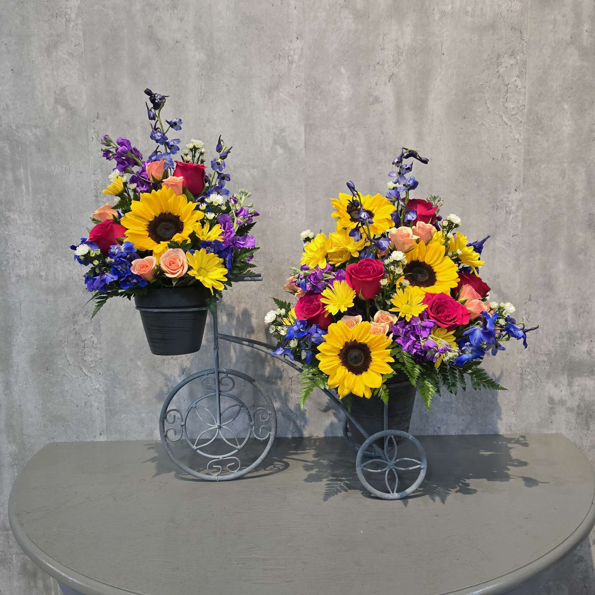 Two colorful flower arrangements in black pots on decorative metal stands.