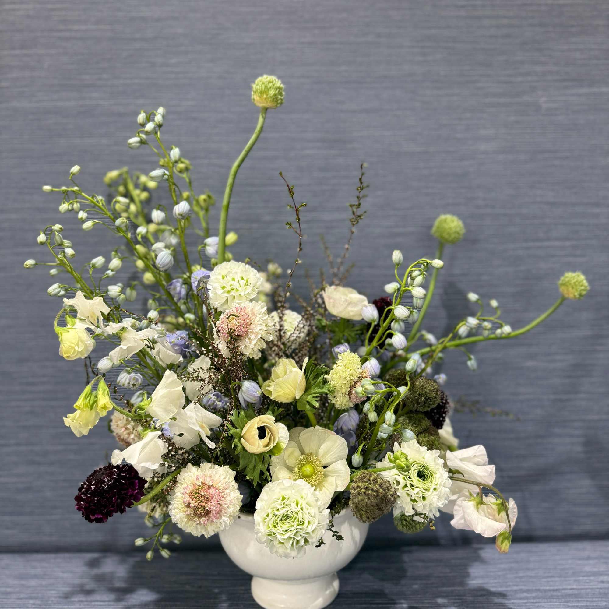 A lush, garden-gathered arrangement in a white ceramic compote featuring white anemones, photo 2 of 2