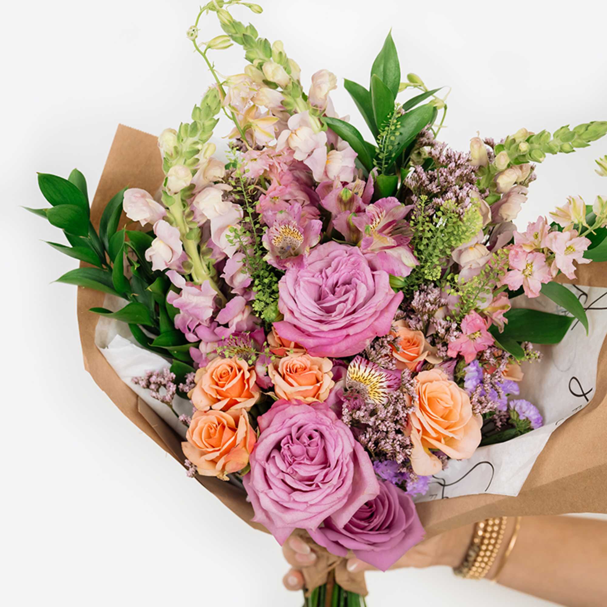 Handheld bouquet of pink and peach roses with mixed pastel flowers