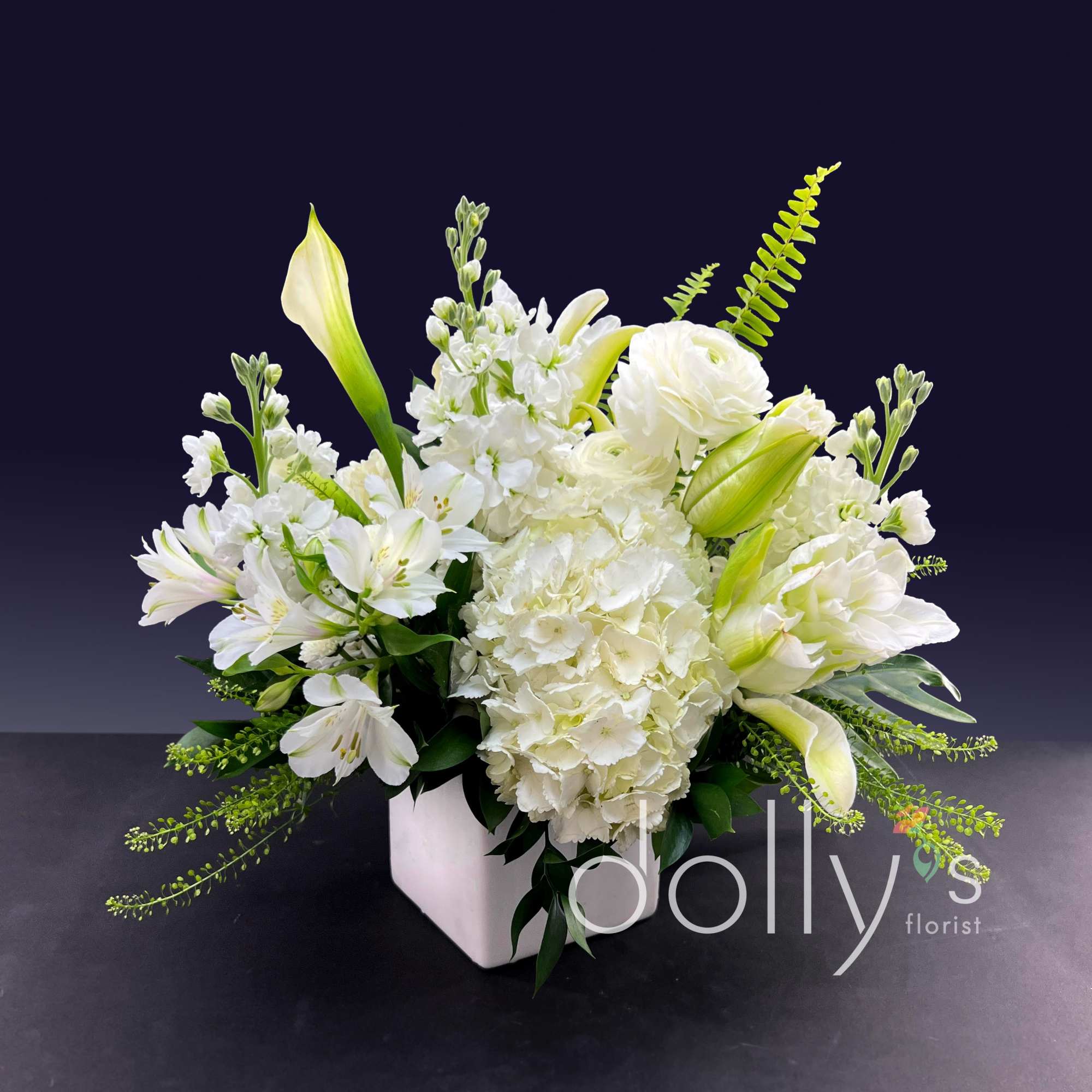 White floral arrangement in a square vase with lilies and hydrangeas