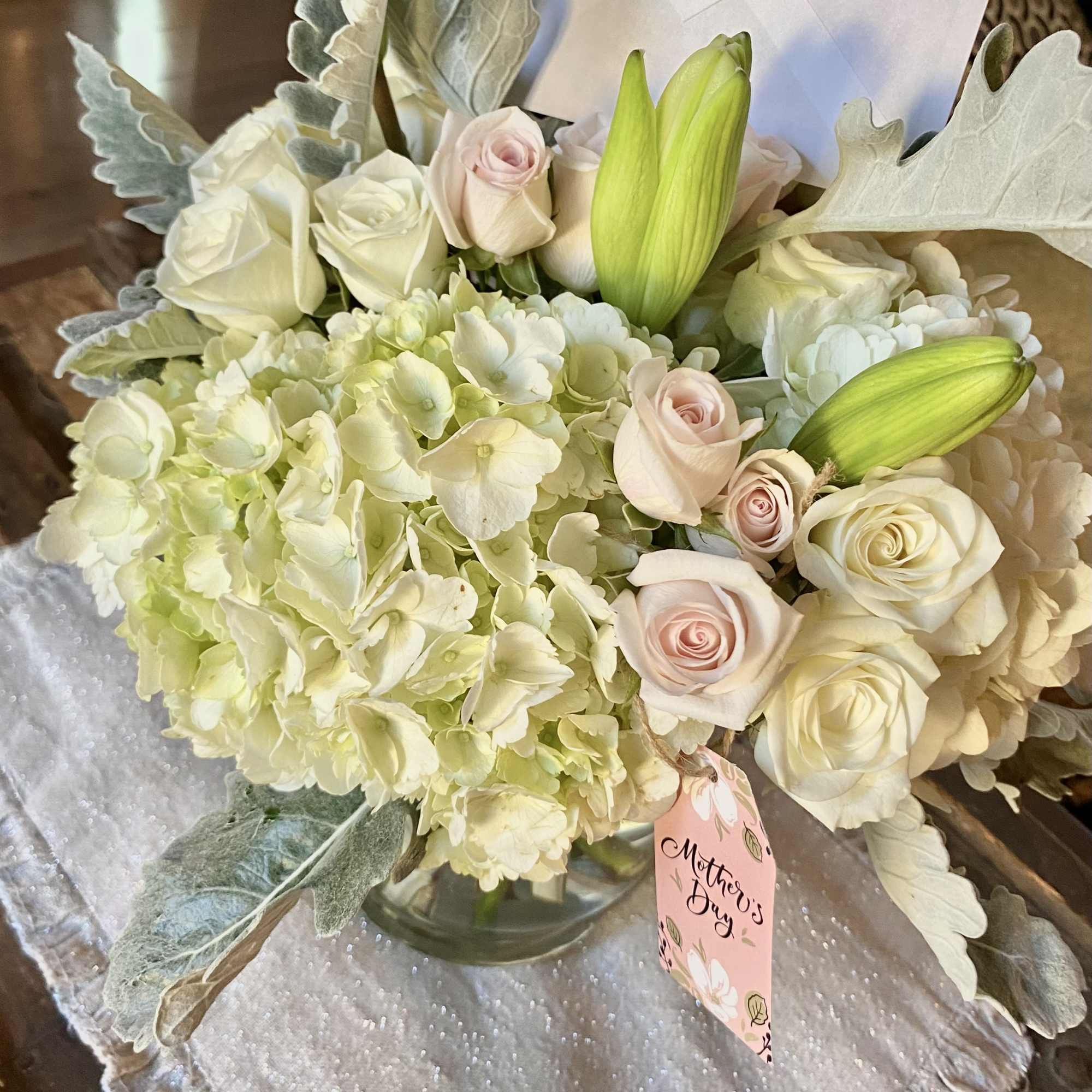 Bouquet of pale roses, hydrangeas, and lily buds in a glass vase