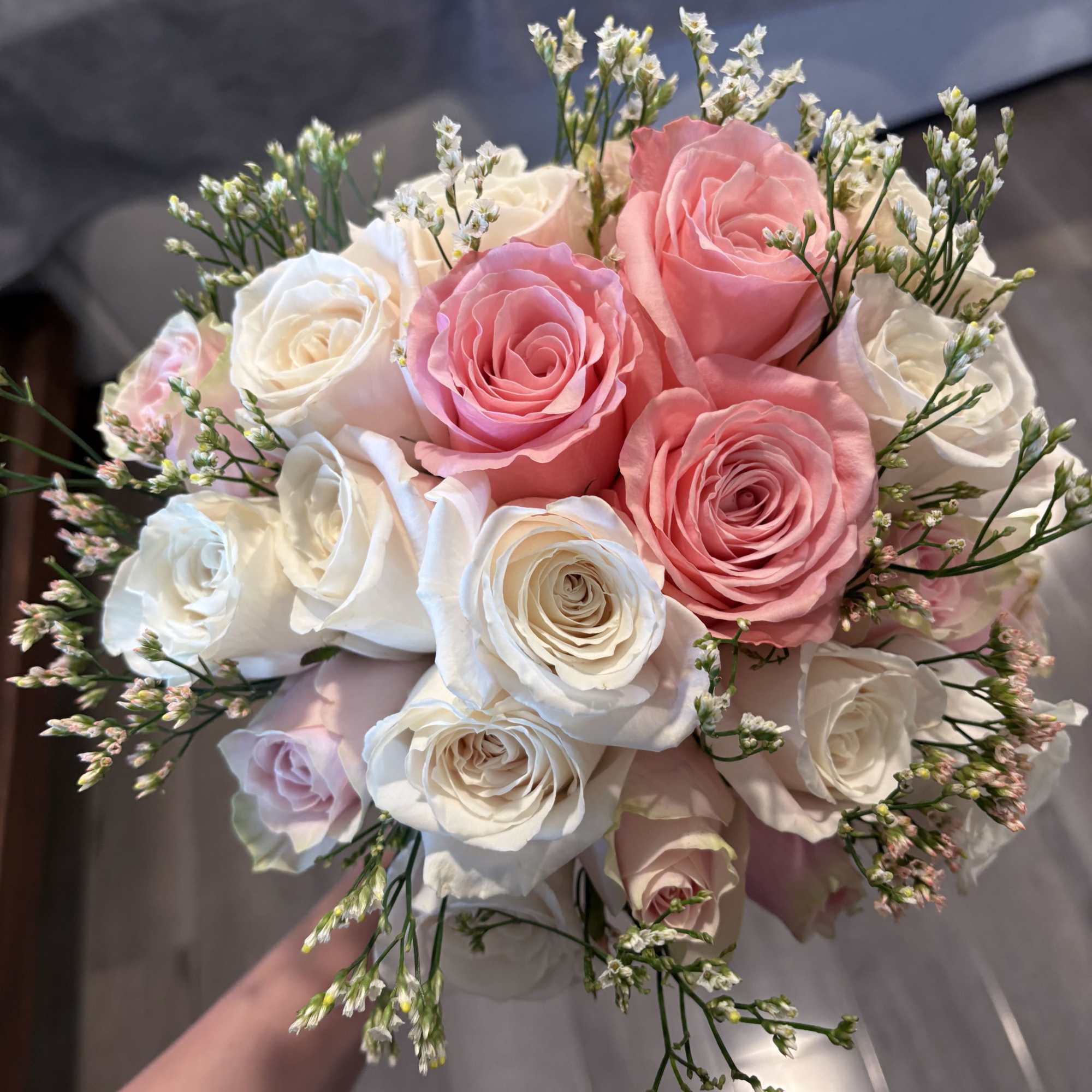 Handheld bouquet of pink and white roses with small filler flowers