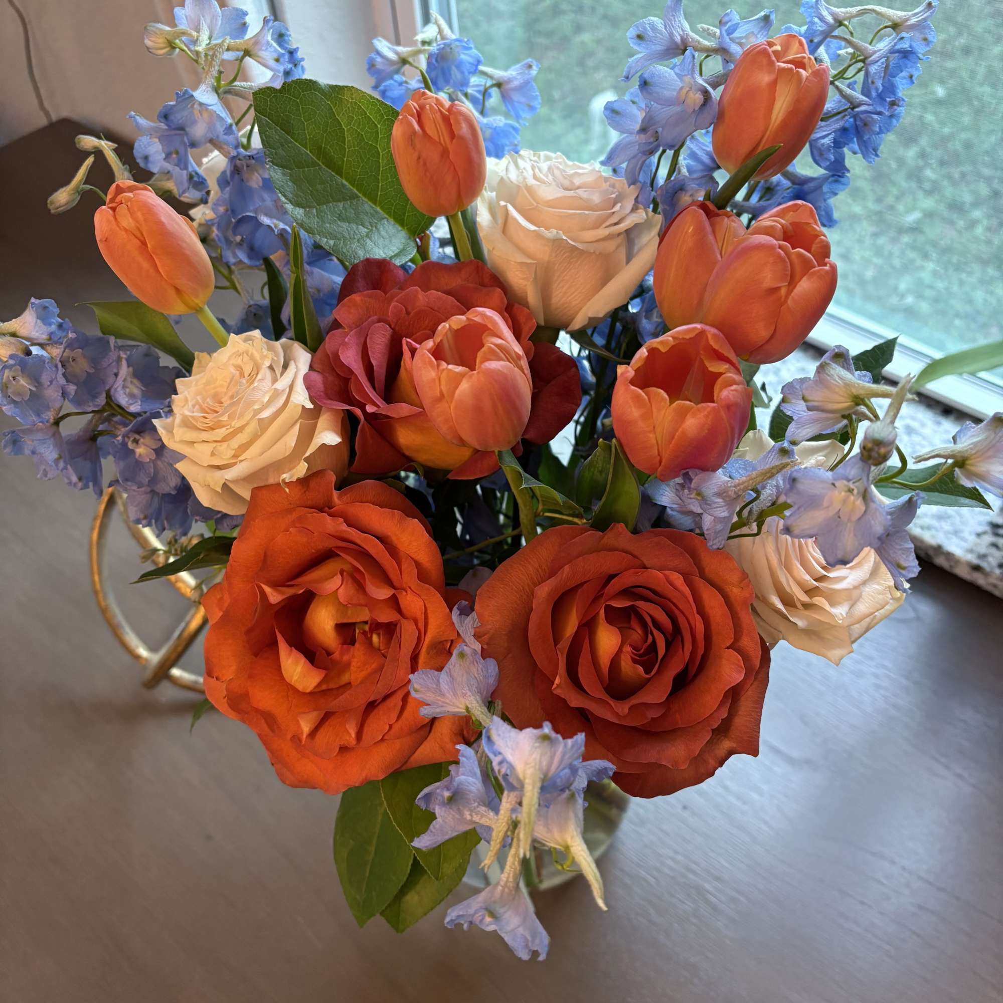 Bouquet of orange roses, cream roses, and blue flowers in a vase