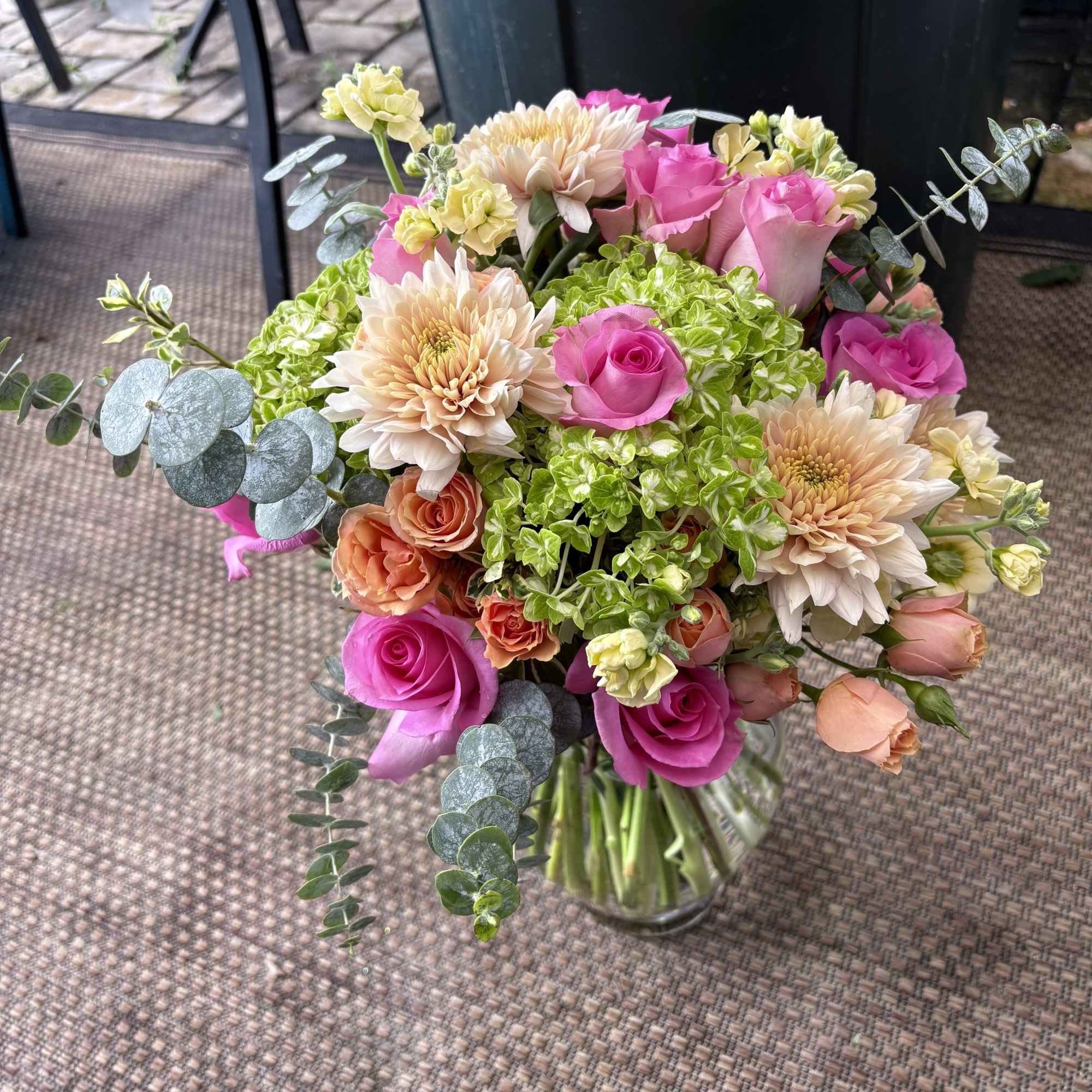 Bouquet of pink roses, peach dahlias, and green hydrangeas in a glass vase