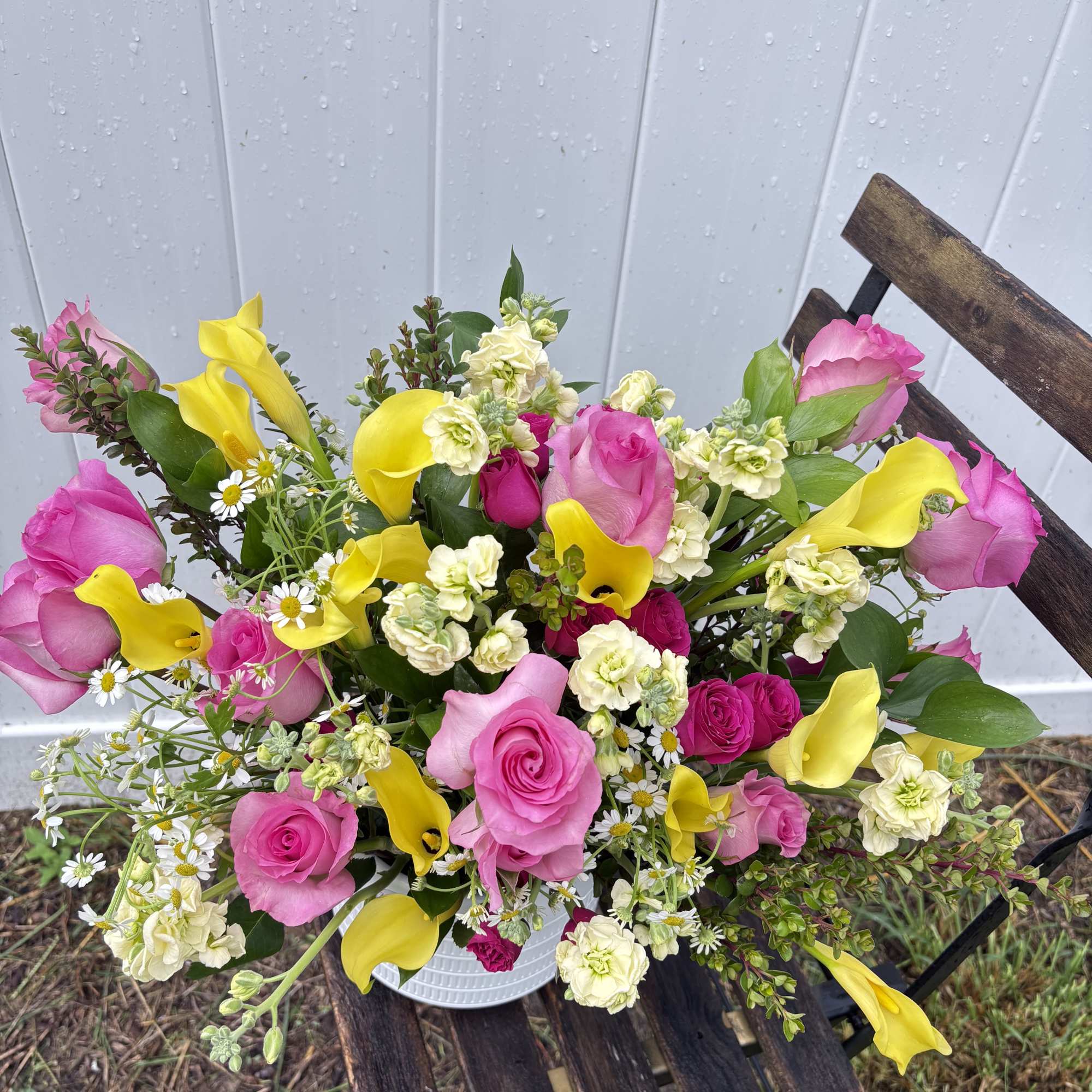 Bouquet of pink roses, yellow calla lilies, and small white flowers in a white container