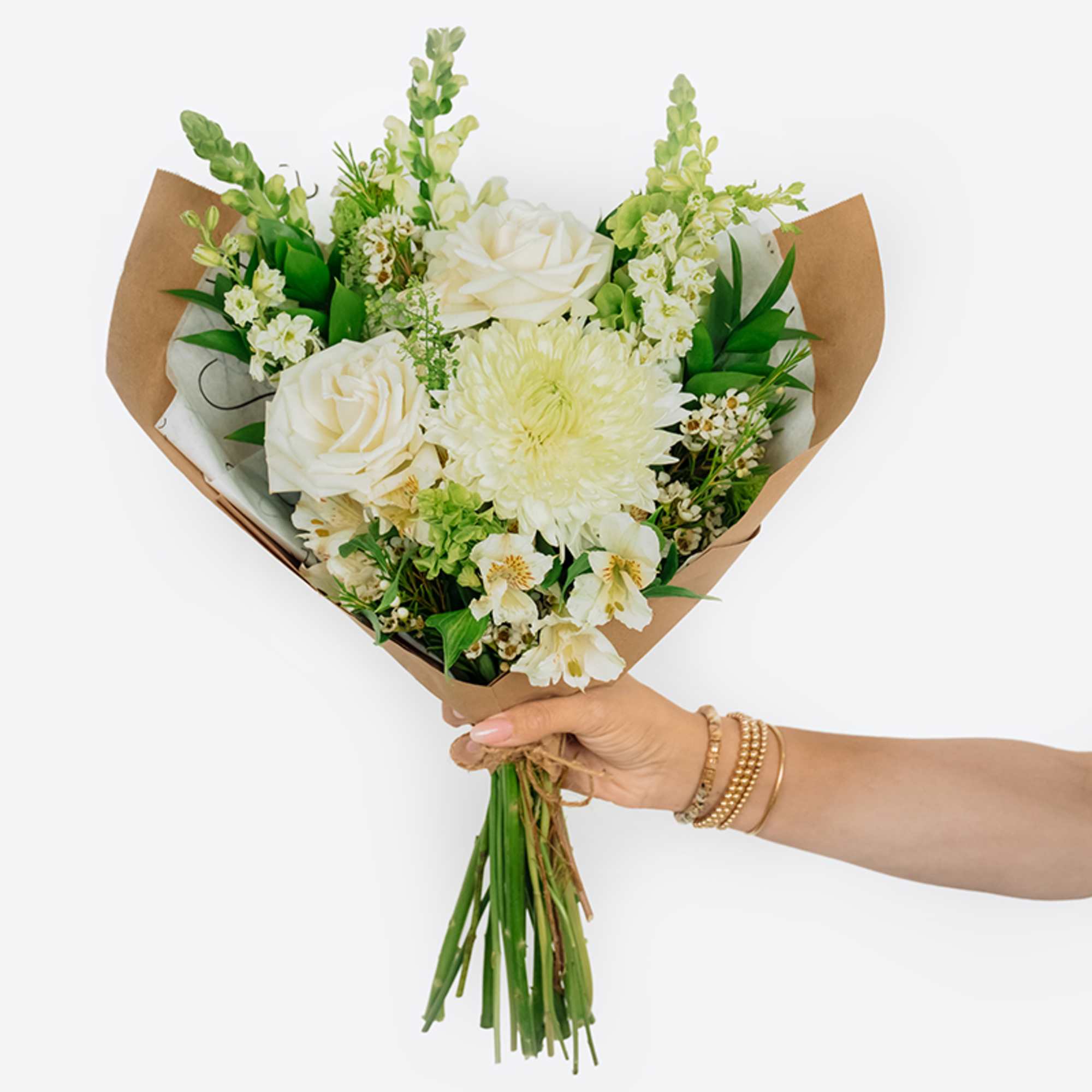 Handheld bouquet of white roses and pale blooms wrapped in brown paper