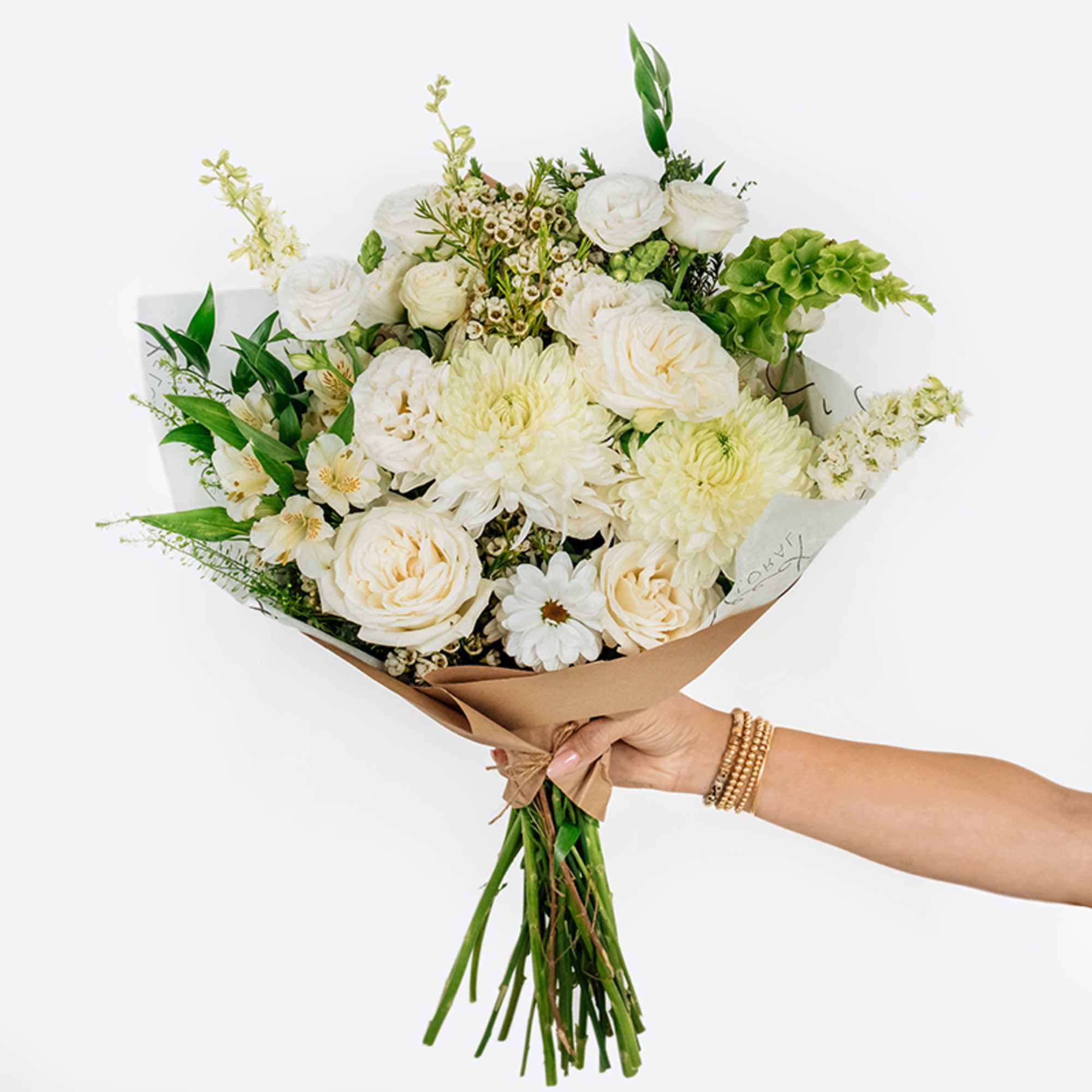 Handheld bouquet of white and cream flowers wrapped in brown paper