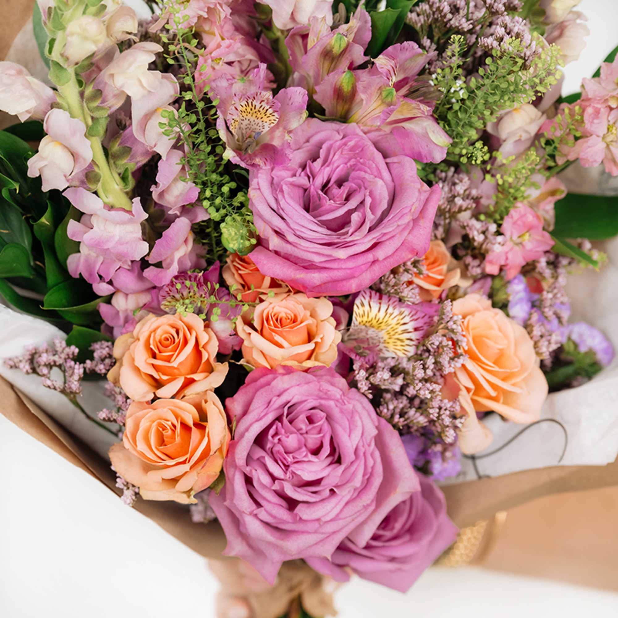 Bouquet of pink and peach roses with mixed blooms wrapped in paper