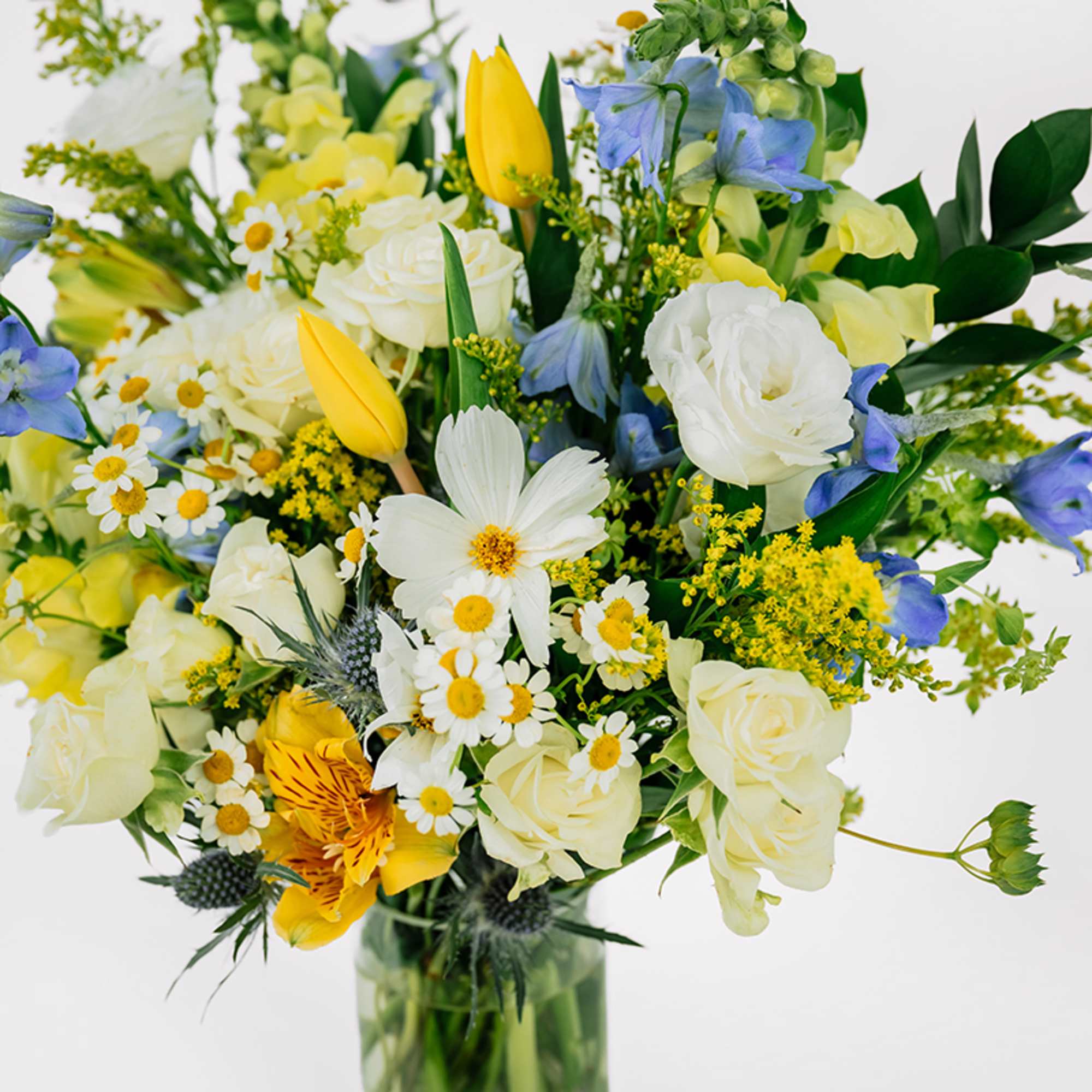 Mixed bouquet of white, yellow, and blue flowers in a glass vase