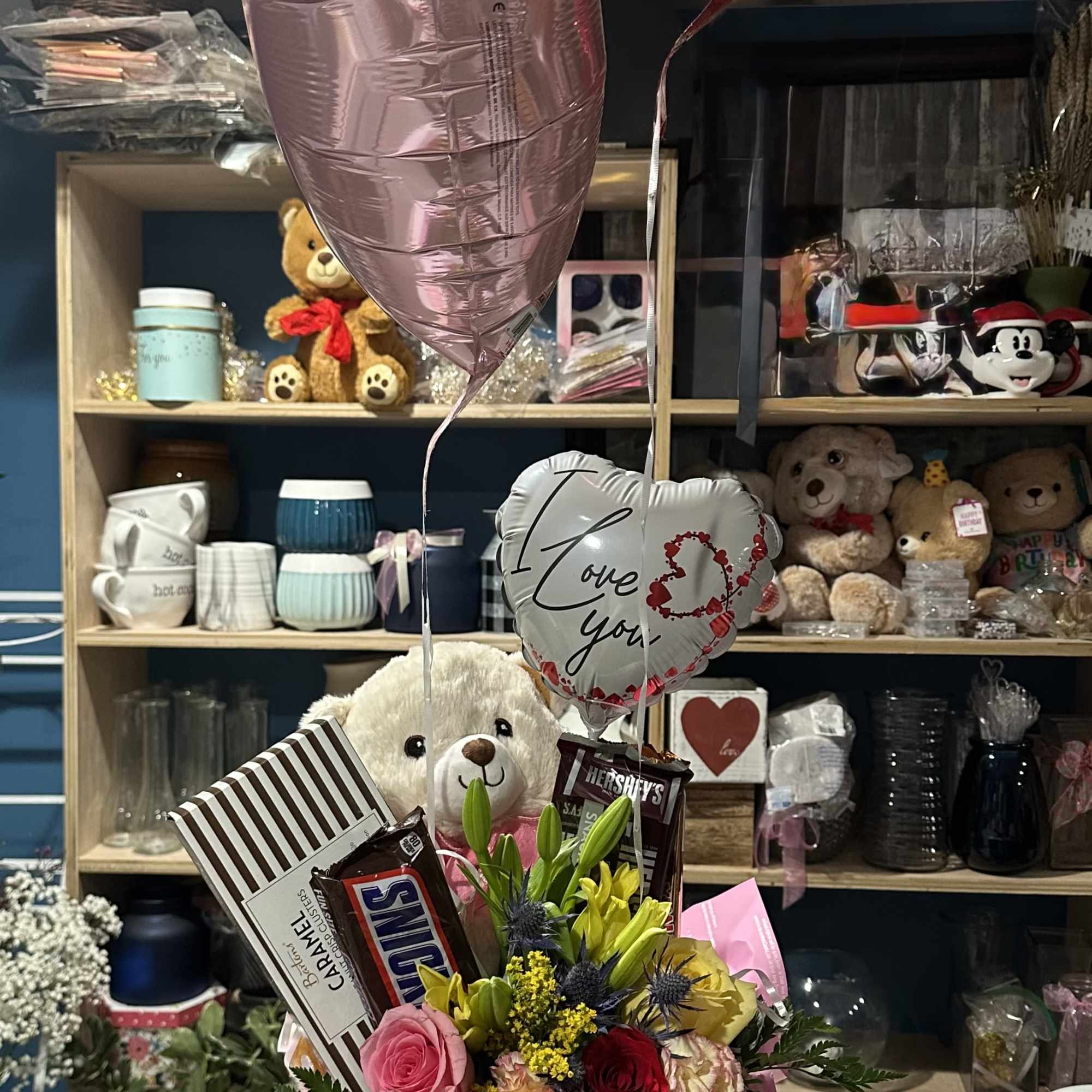 Gift bouquet with roses, lilies, chocolates, a teddy bear, and heart balloons